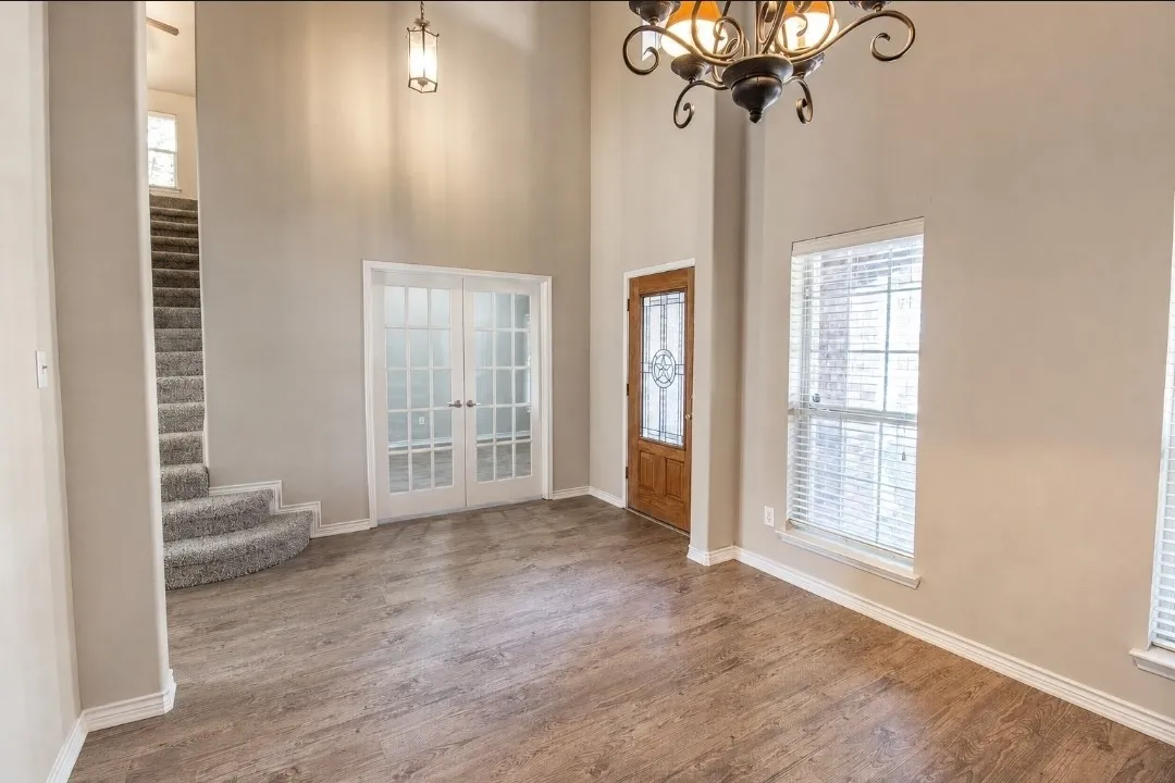 Two-story foyer featuring wood-finish flooring, a decorative chandelier, and a wood entry door with leaded glass