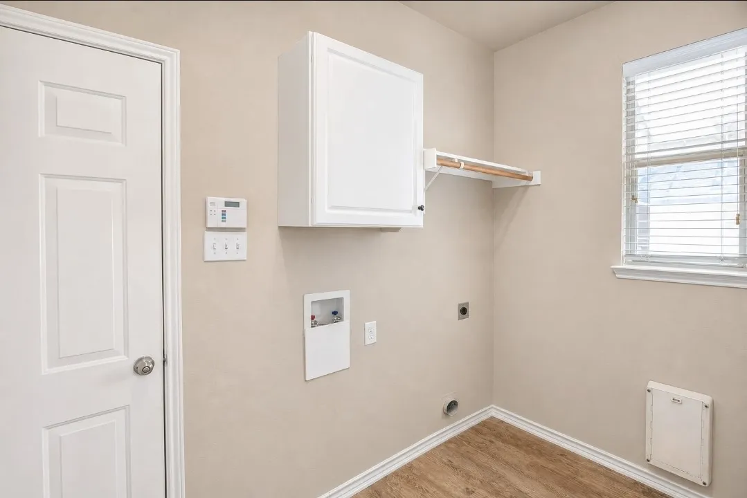 Wood-finish flooring, white paneled door, white cabinetry, integrated wall shelving, and a single window with blinds