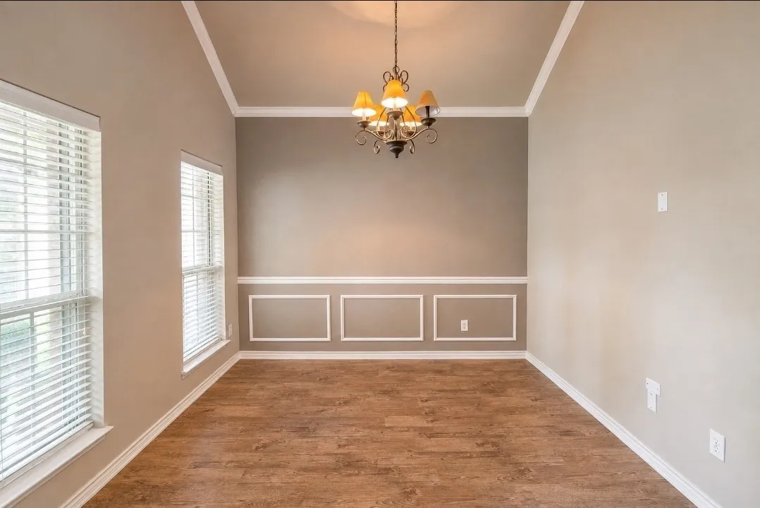 Tray ceiling with crown molding, decorative wainscoting, wood-finish flooring, two windows with blinds, and a five-light chandelier