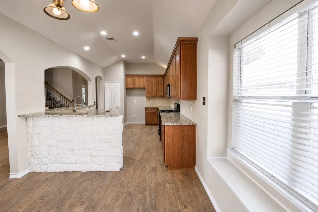 Kitchen featuring wood-finish flooring, recessed lighting, wood cabinetry, stone countertops, and an arched architectural opening