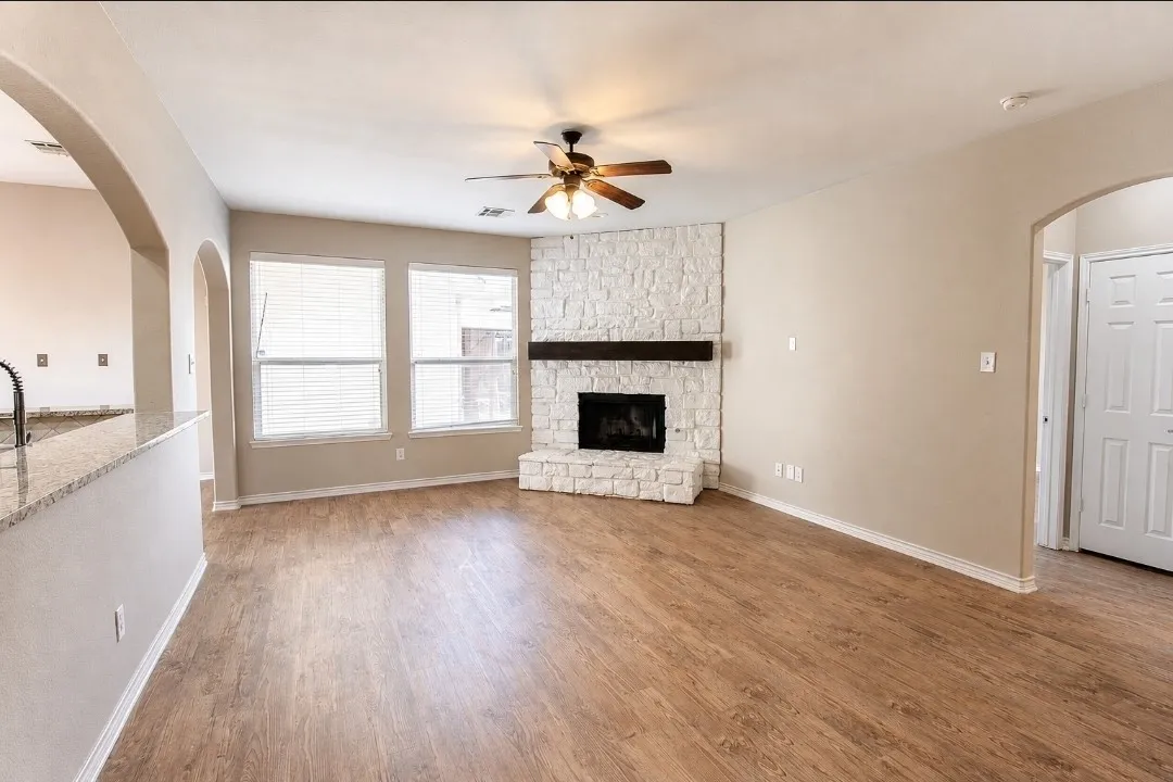 Living area featuring wood-finish flooring, a stone-clad fireplace with a wood mantel, and multiple windows