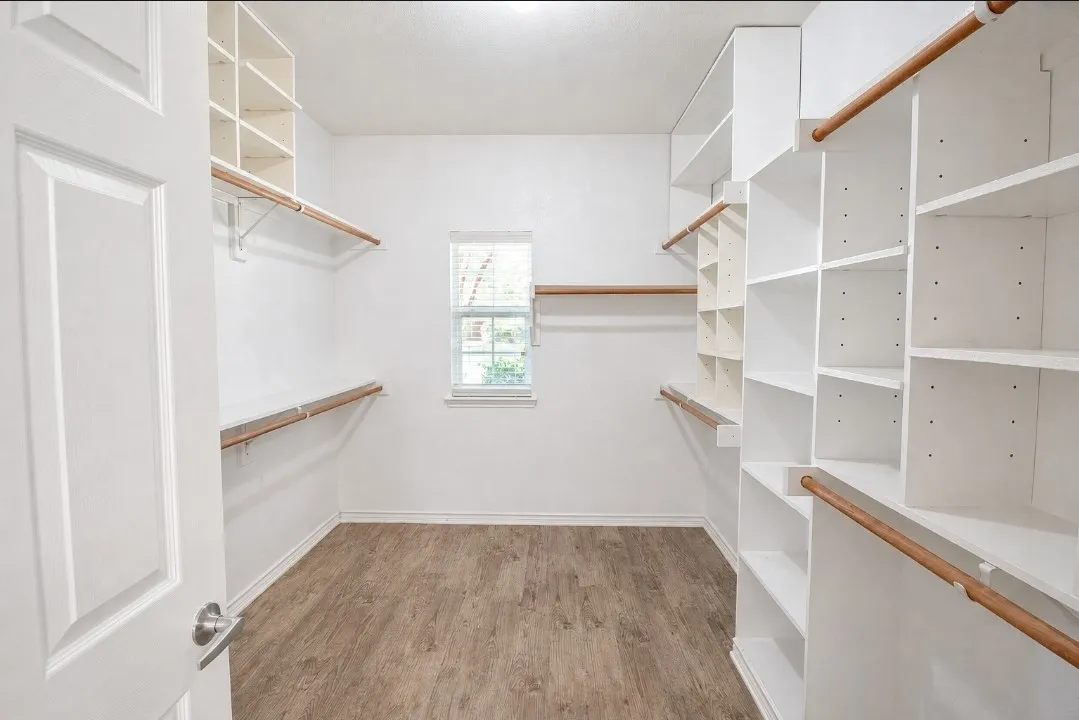 Spacious walk-in closet featuring built-in shelving, hanging rods, wood-finish flooring, and a natural light window