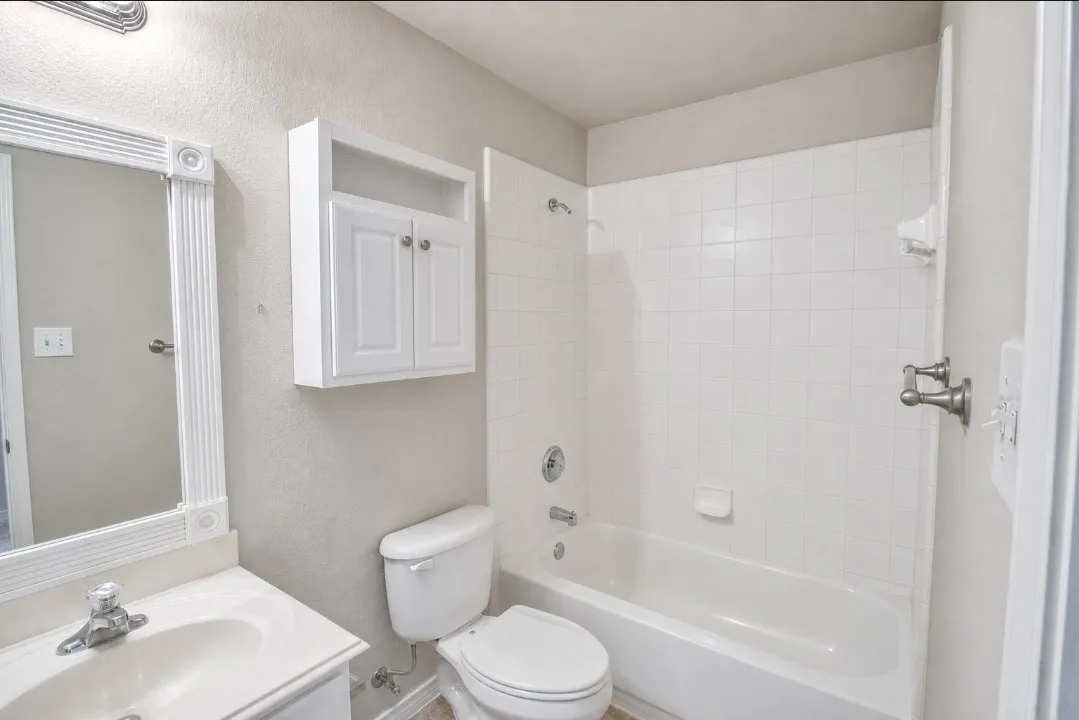 Bathroom featuring a white vanity with integrated sink, a framed mirror, a wall-mounted cabinet, and a white tiled shower-tub combination