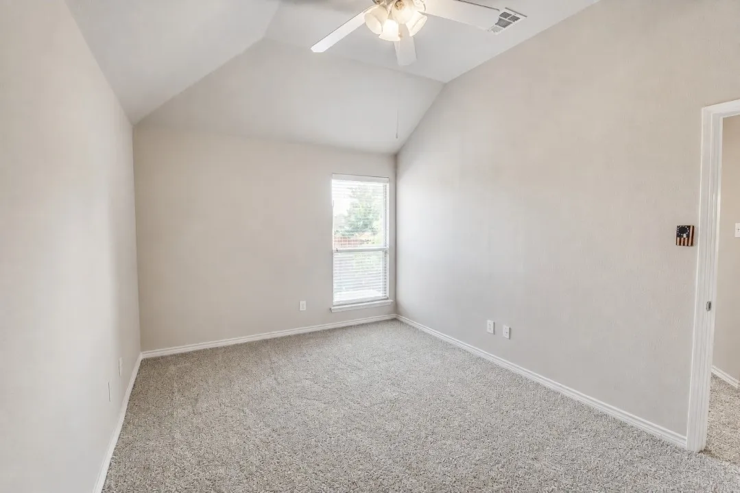 Sloped ceiling with an attached ceiling fan, carpet flooring, and a single window with blinds