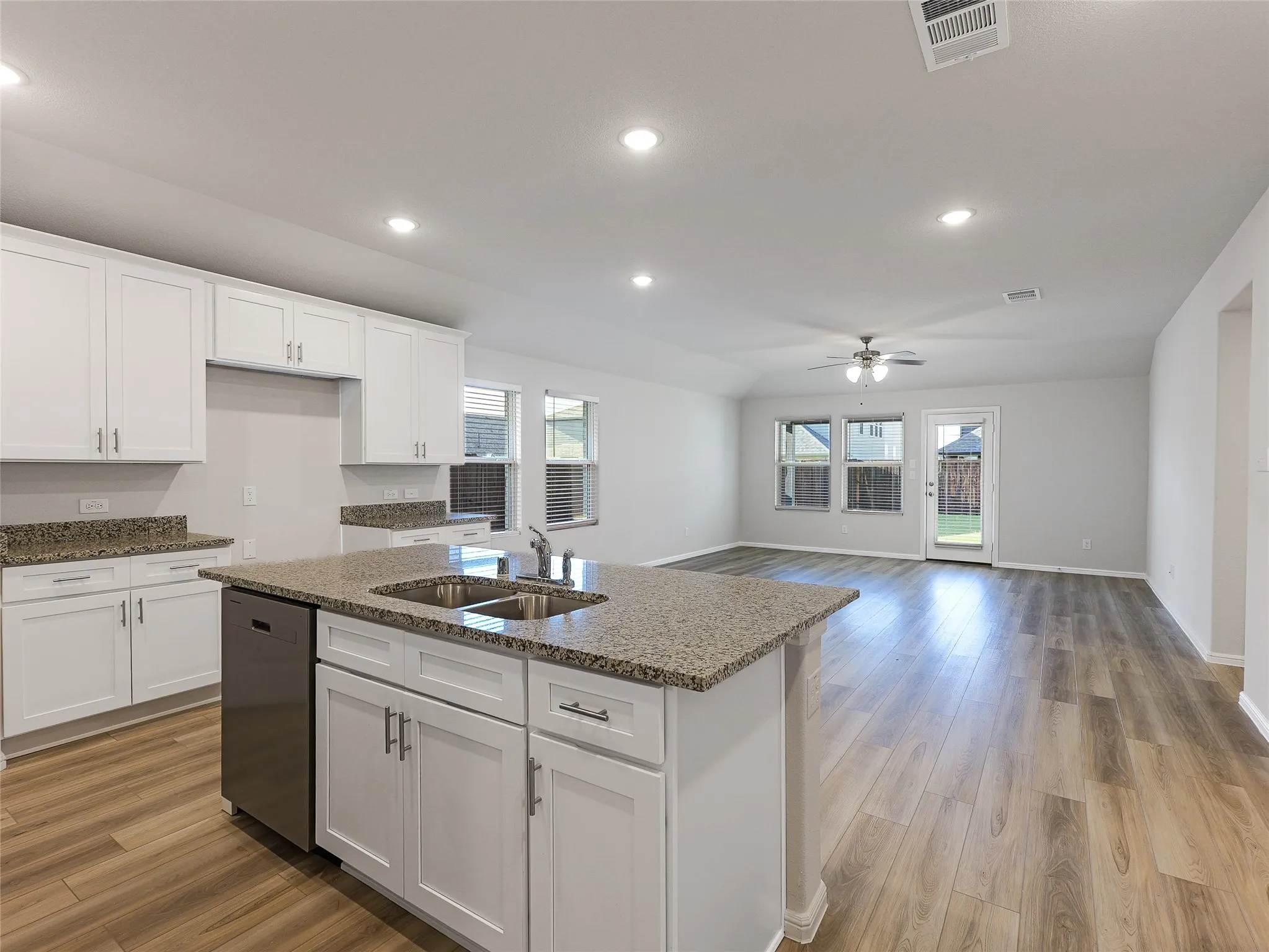 Open-concept kitchen and living area featuring white cabinetry, granite countertops, a center island with storage, stainless steel appliances, recessed lighting, wood-finish flooring, and French doors leading to the backyard