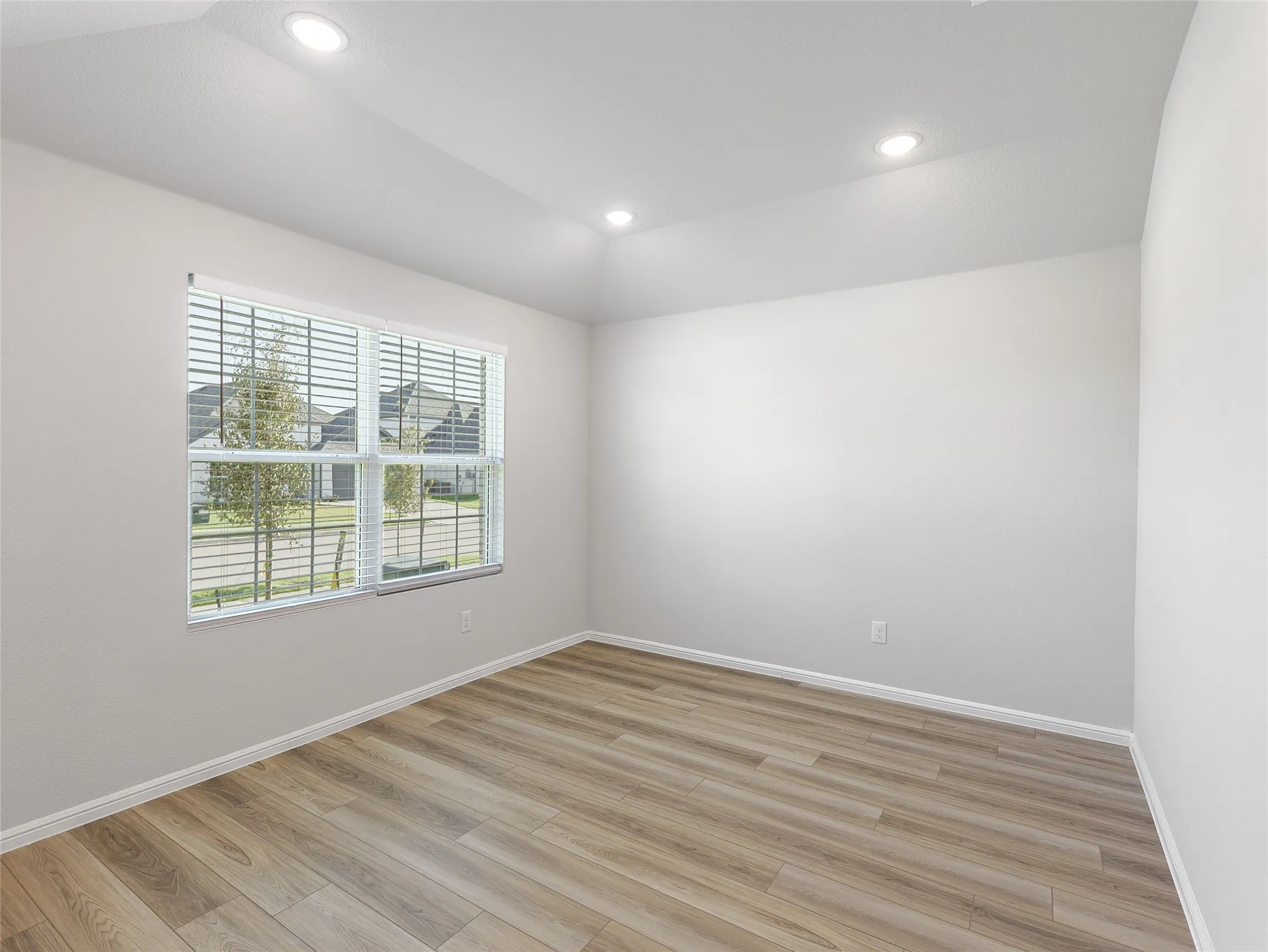 Bright, light-filled bedroom featuring recessed ceiling lighting, large double-hung windows with plantation shutters, and warm wood-finish flooring throughout