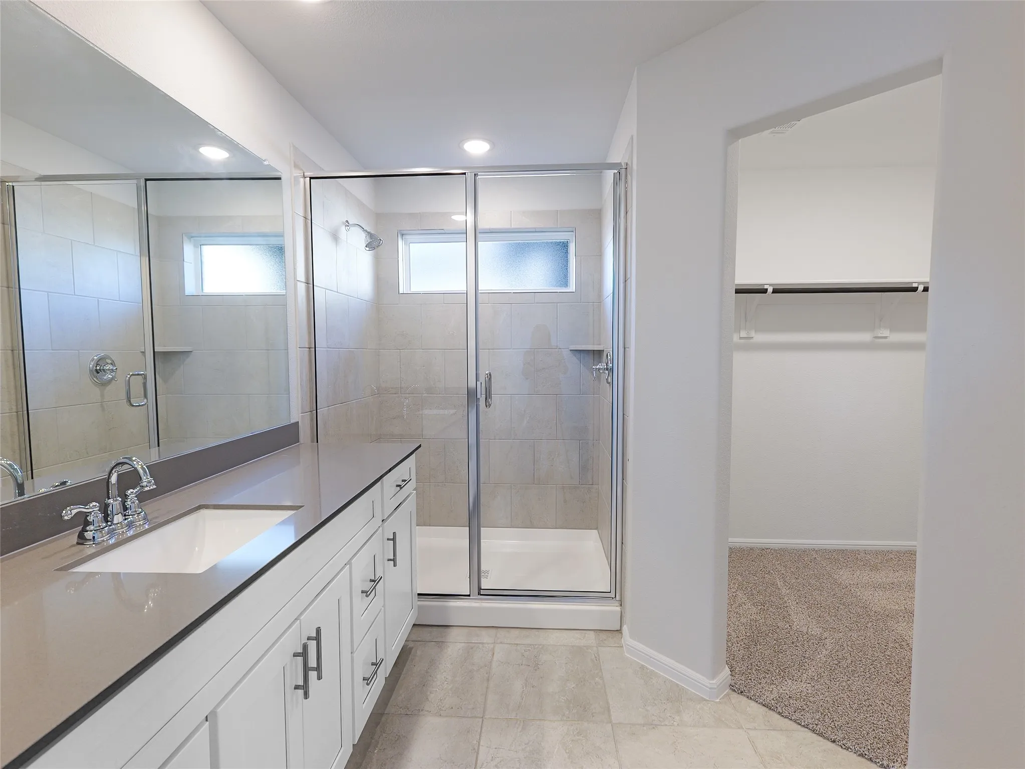 Vanity with a single undermount sink, a glass-enclosed shower, tiled flooring, and recessed lighting
