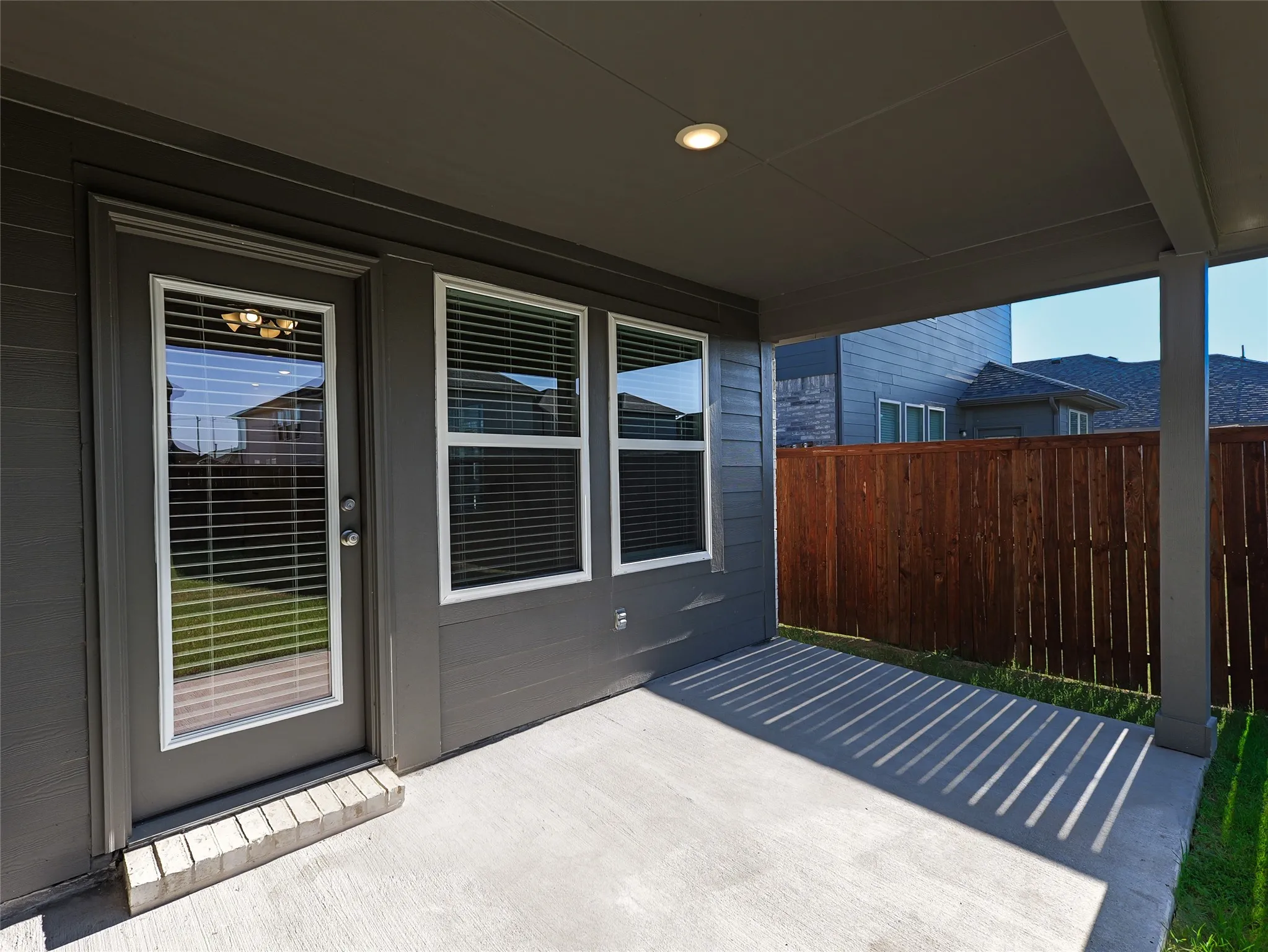 Covered patio with composite decking and aluminum railings, featuring multiple sliding glass doors and windows with horizontal blinds
