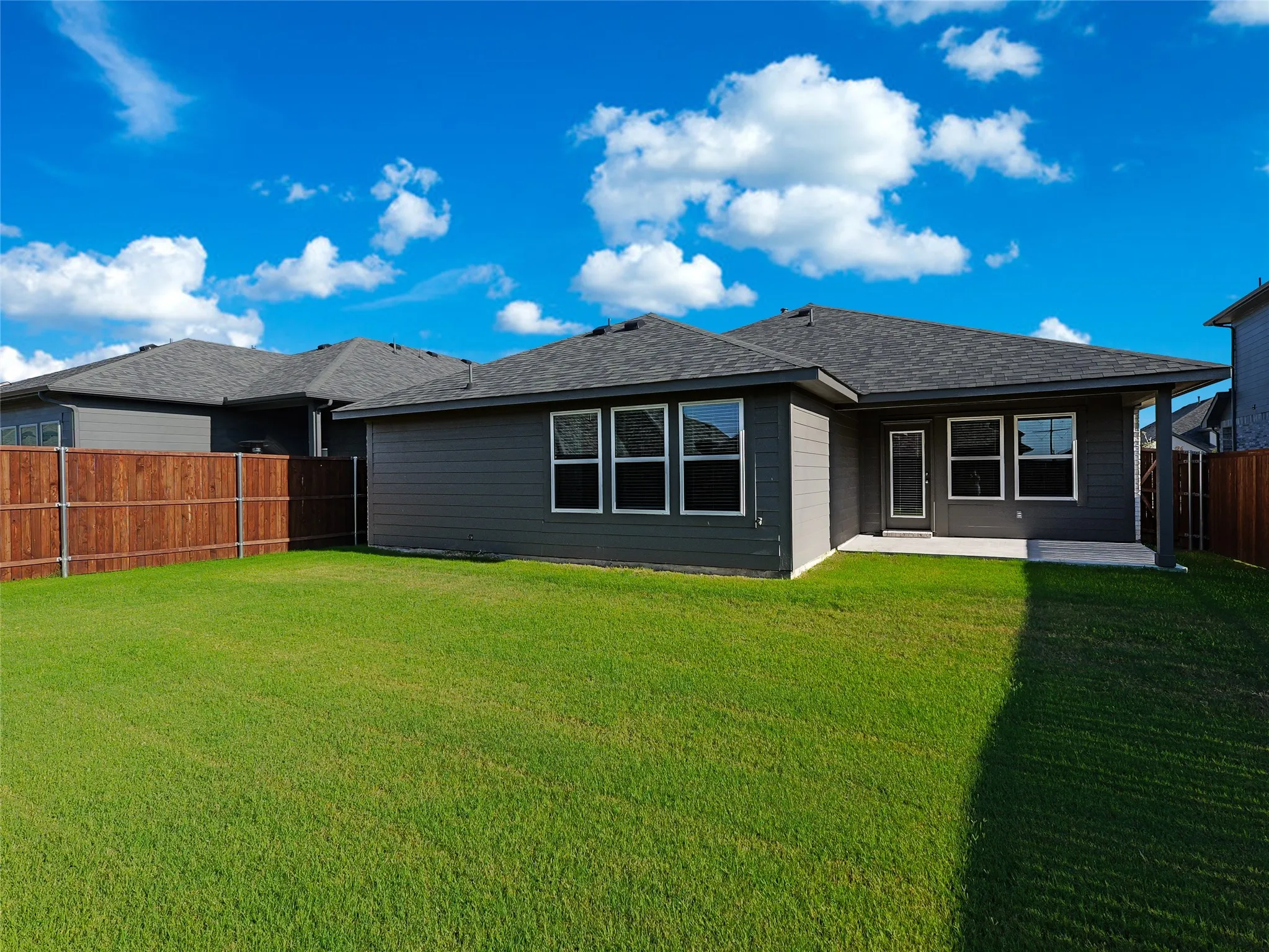 Expansive rear yard with a wood privacy fence, covered patio, and multiple windows