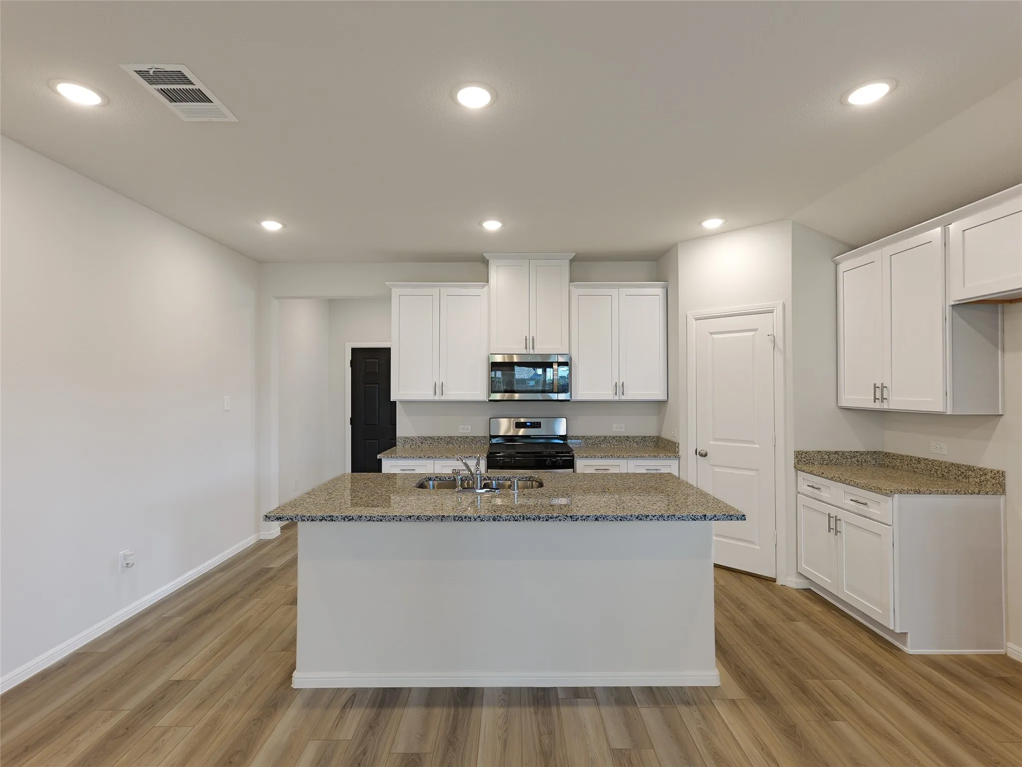 Modern kitchen featuring white cabinetry, granite countertops, stainless steel appliances, a substantial island with seating, and warm wood-finish flooring throughout the open-concept space