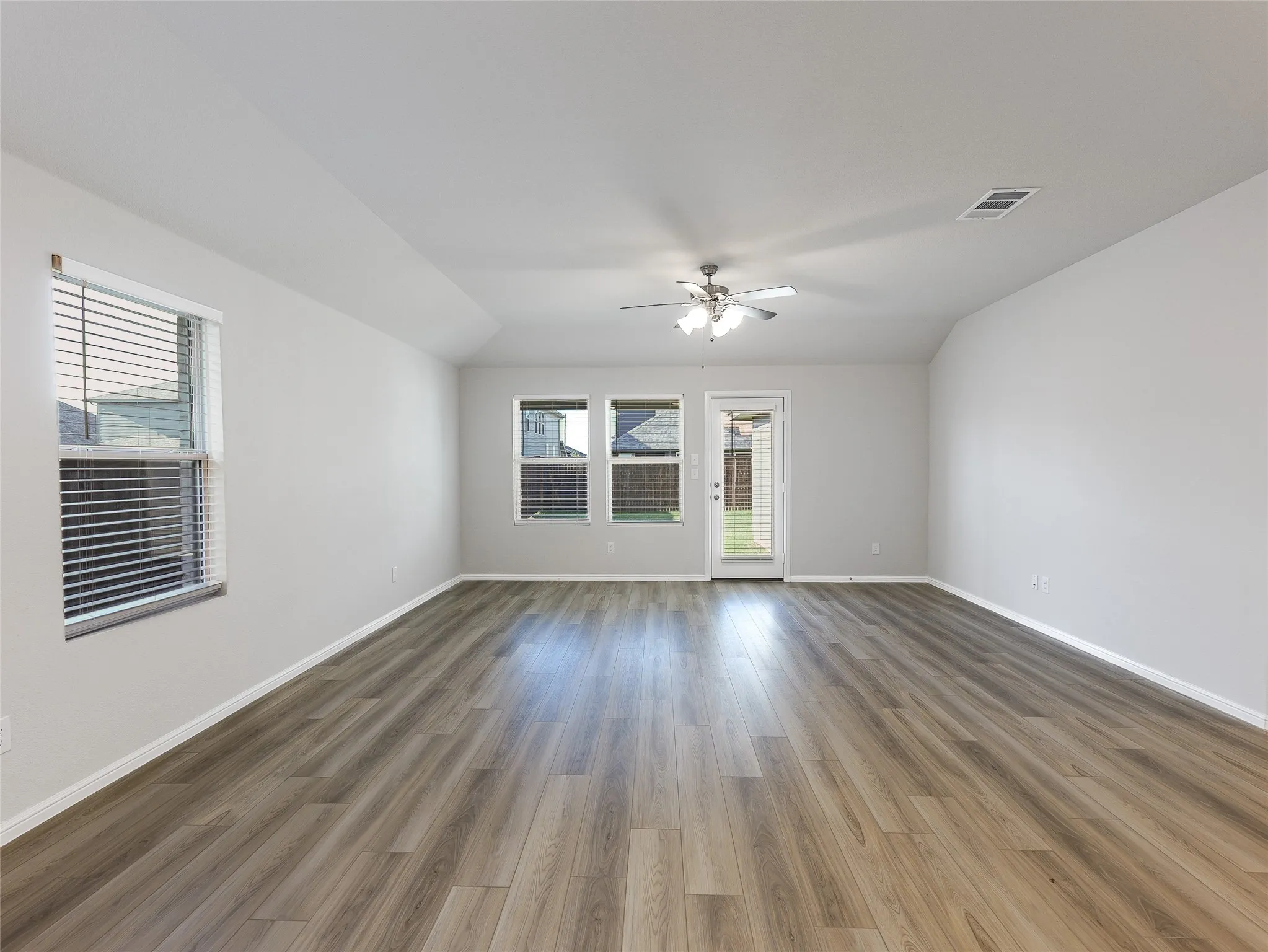 Spacious room with engineered wood-finish flooring, white walls, and ceiling fan with integrated lighting