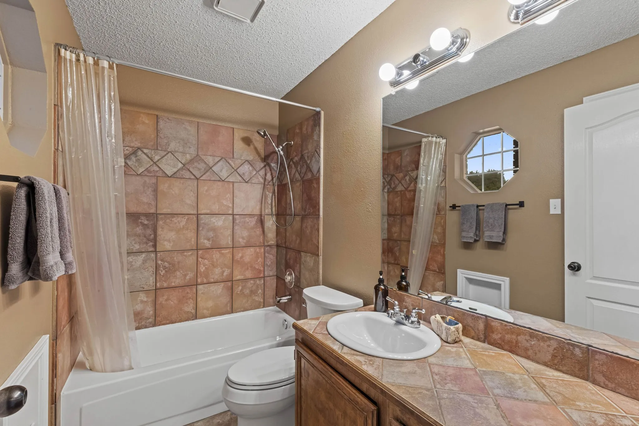 Bathroom featuring a tiled tub surround, integrated shower, vanity with an integrated sink, tiled countertop, and an octagonal window