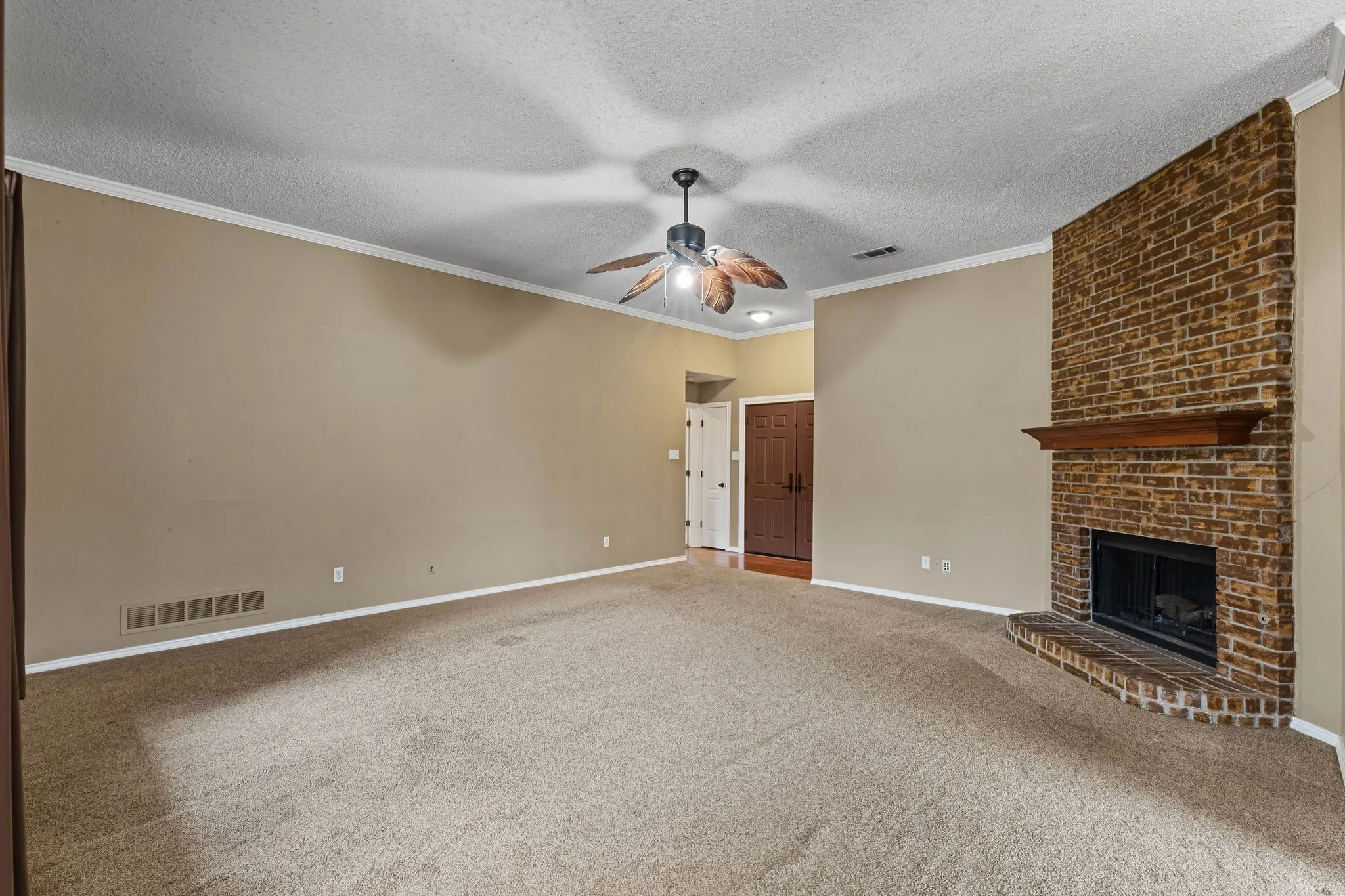 Spacious room featuring a brick fireplace with a wood mantel, crown molding, a ceiling fan, and carpeted flooring
