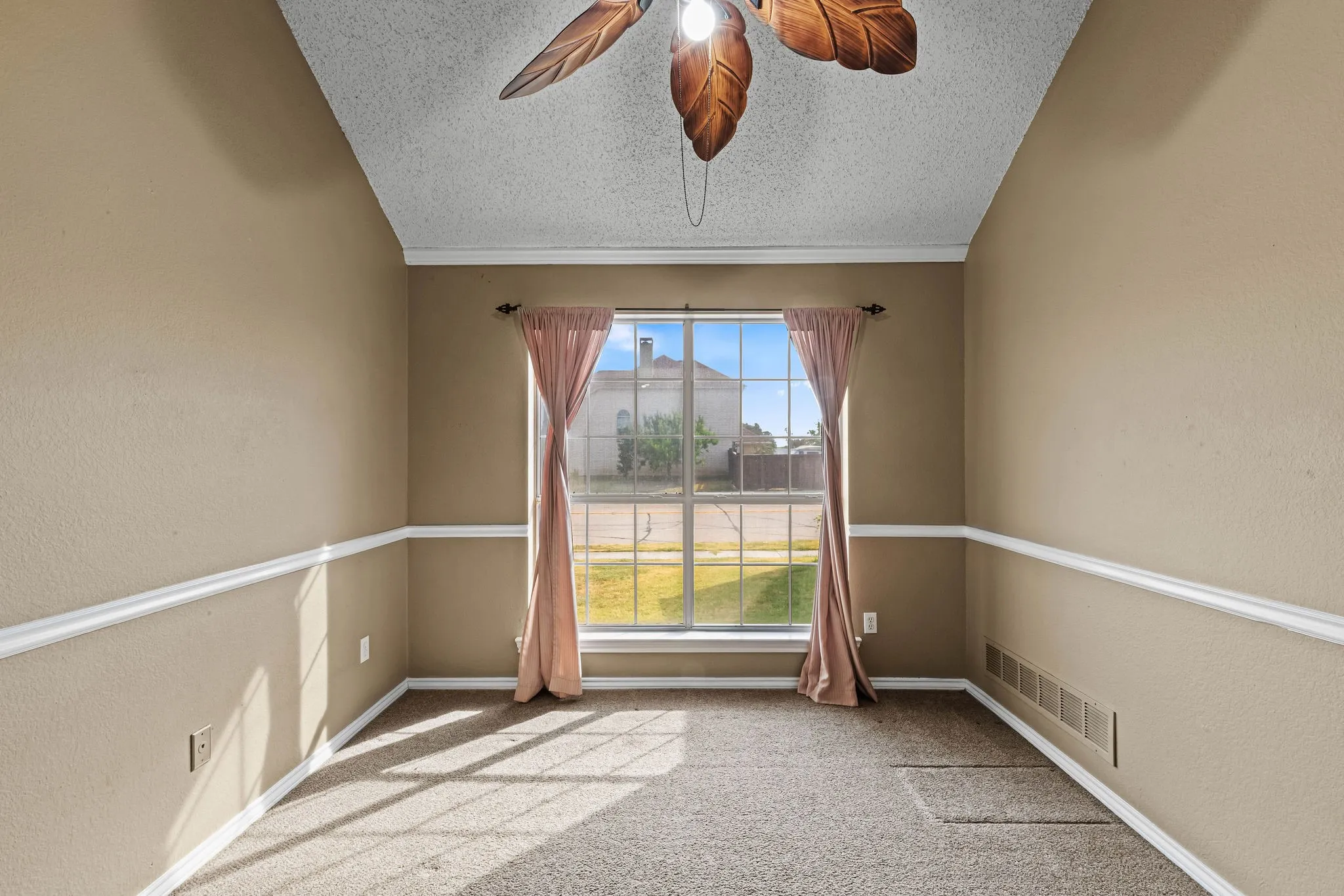 Vaulted ceiling with a decorative ceiling fan, large front-facing window, and chair rail molding