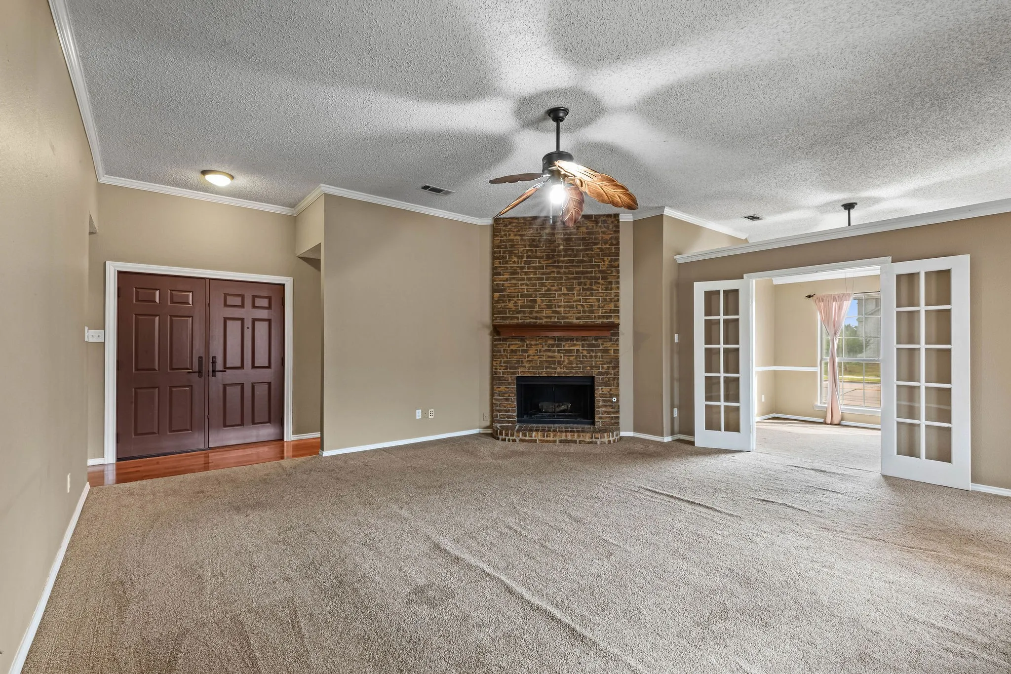 Brick fireplace with a wood-finish mantel, double French doors, double panel entry doors, and crown molding