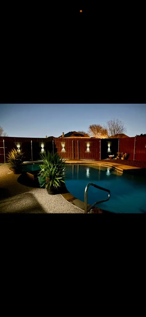 Swimming pool with integrated lighting, perimeter fencing, and concrete decking