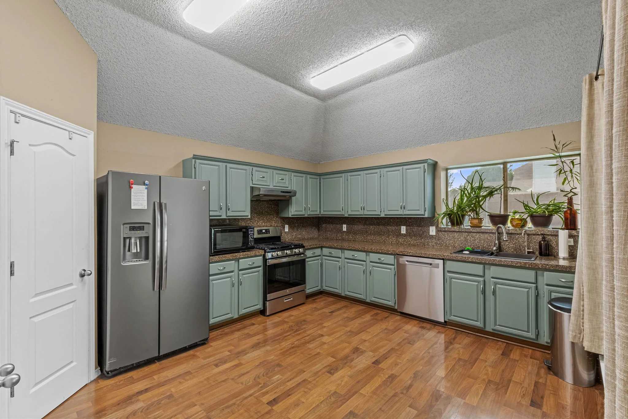 Kitchen featuring wood-finish flooring, L-shaped cabinetry, stainless steel appliances, a double basin sink, and a large window