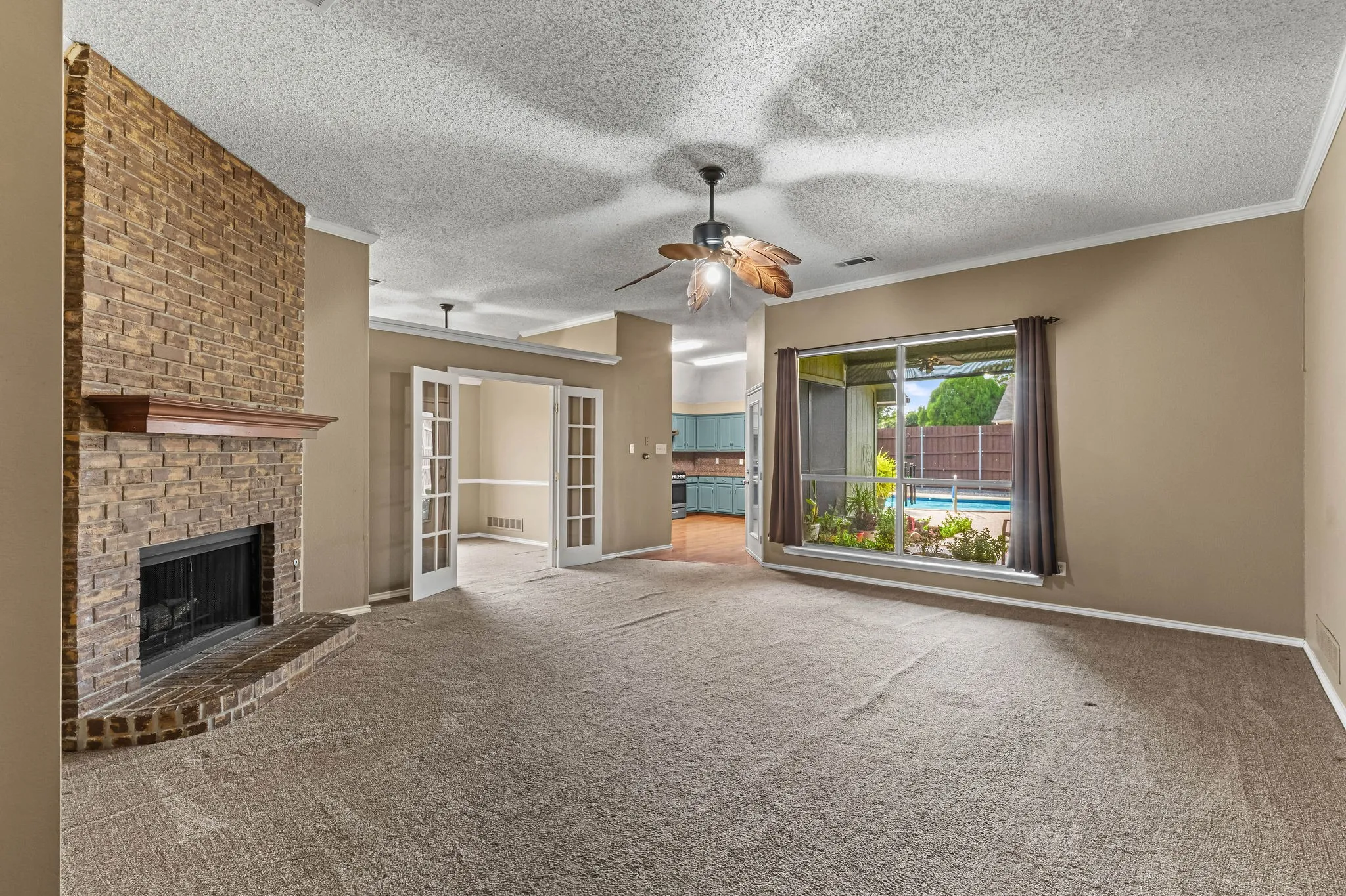 Stone-clad fireplace with mantel, French doors, ceiling fan, and a large window overlooking a pool