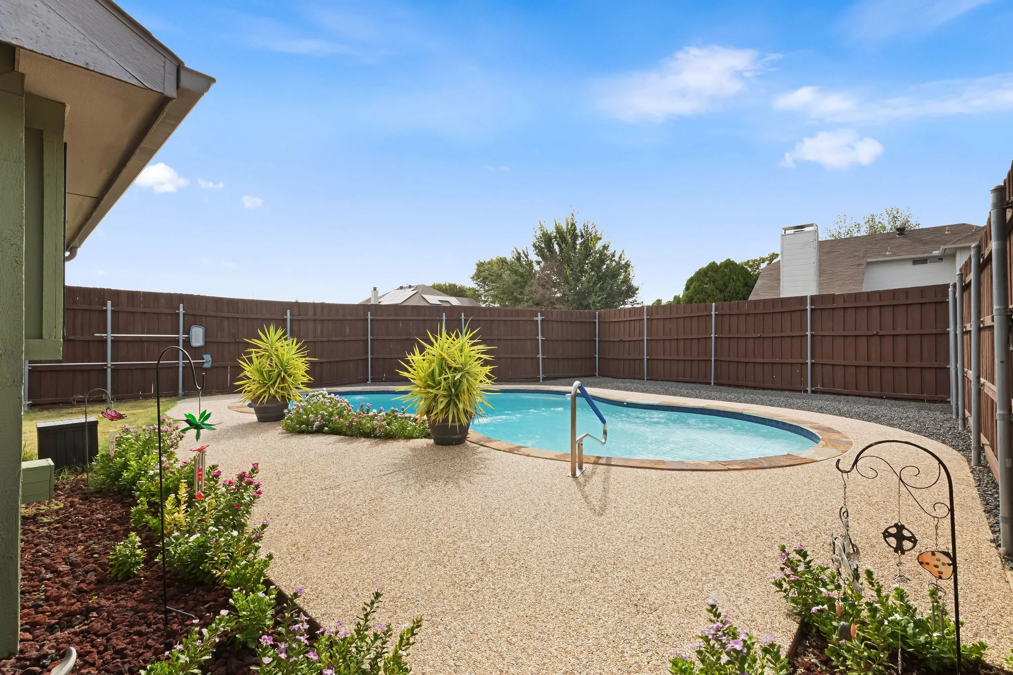 Backyard oasis featuring a curvilinear swimming pool, expansive textured patio, and privacy fencing
