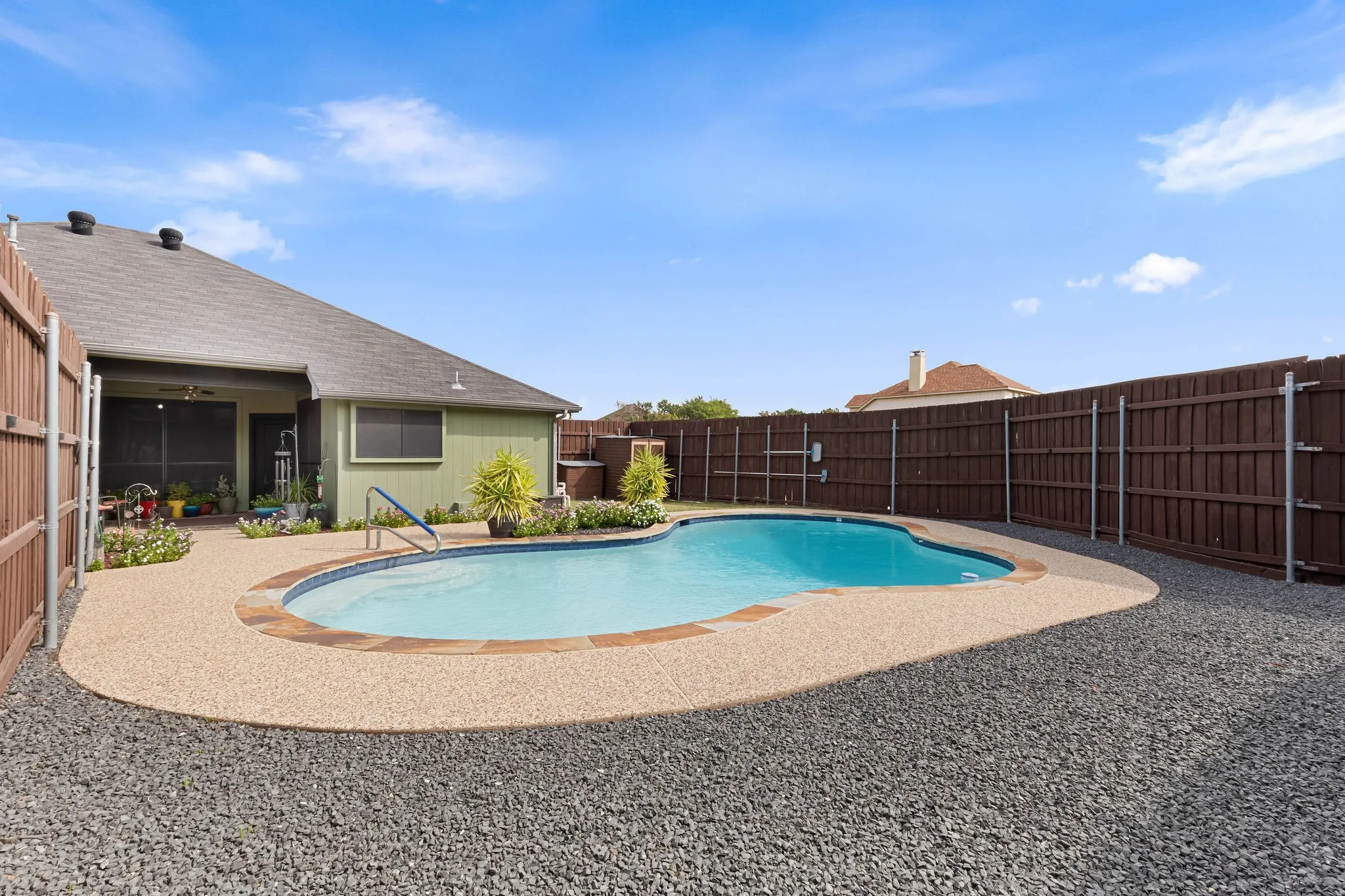 Backyard with a shaped swimming pool, exposed aggregate pool decking, and privacy fencing