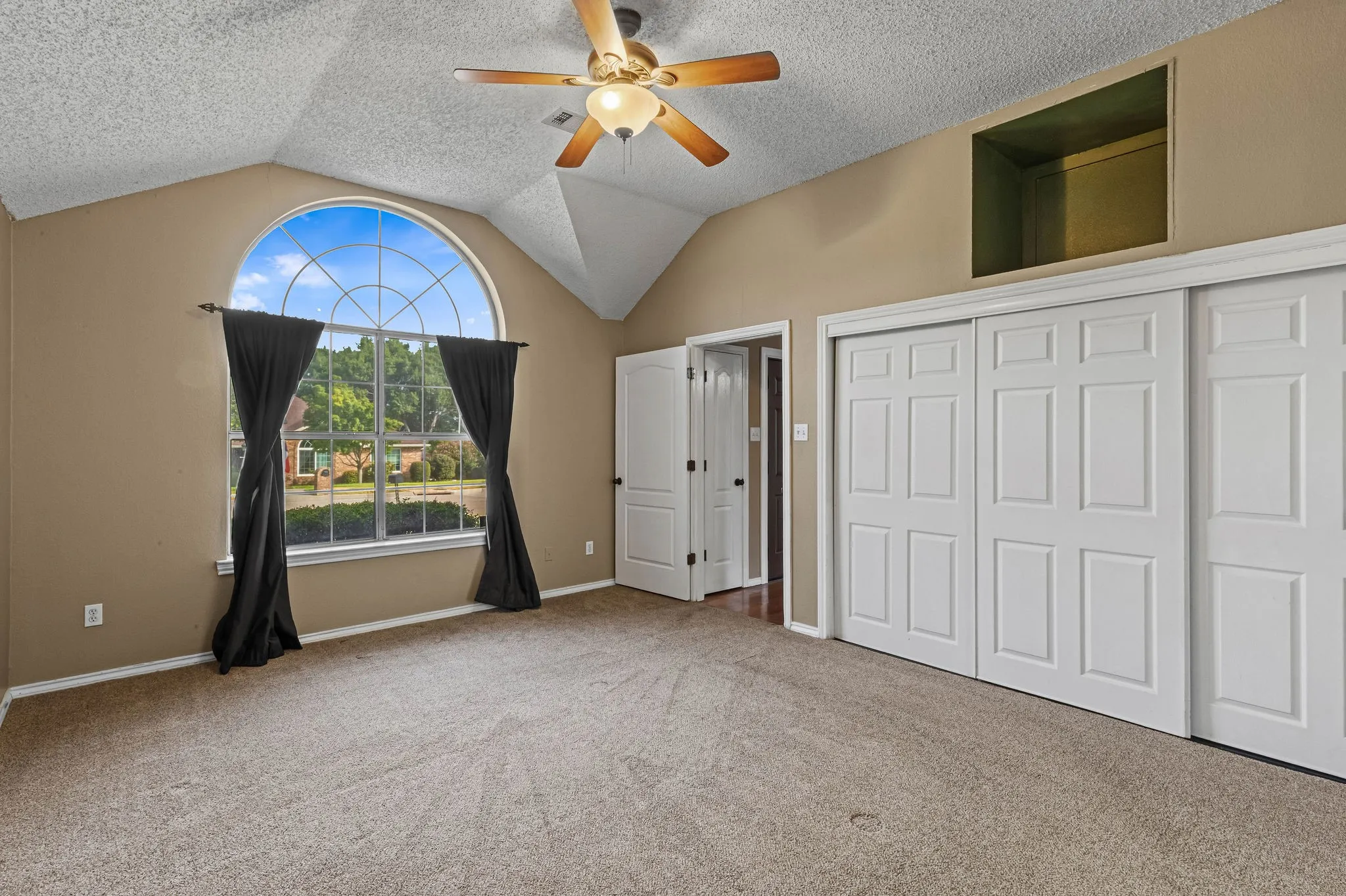 Vaulted ceiling with a ceiling fan, arched window, wall-to-wall carpeting, and white paneled sliding closet doors