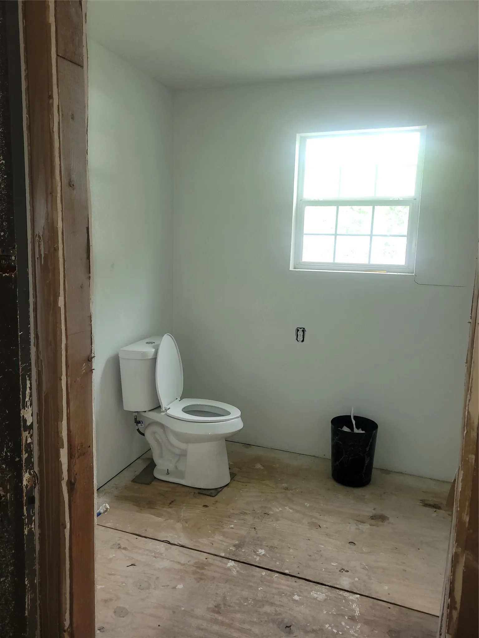 Room featuring a window with a multi-pane grid, white painted walls, and a white toilet