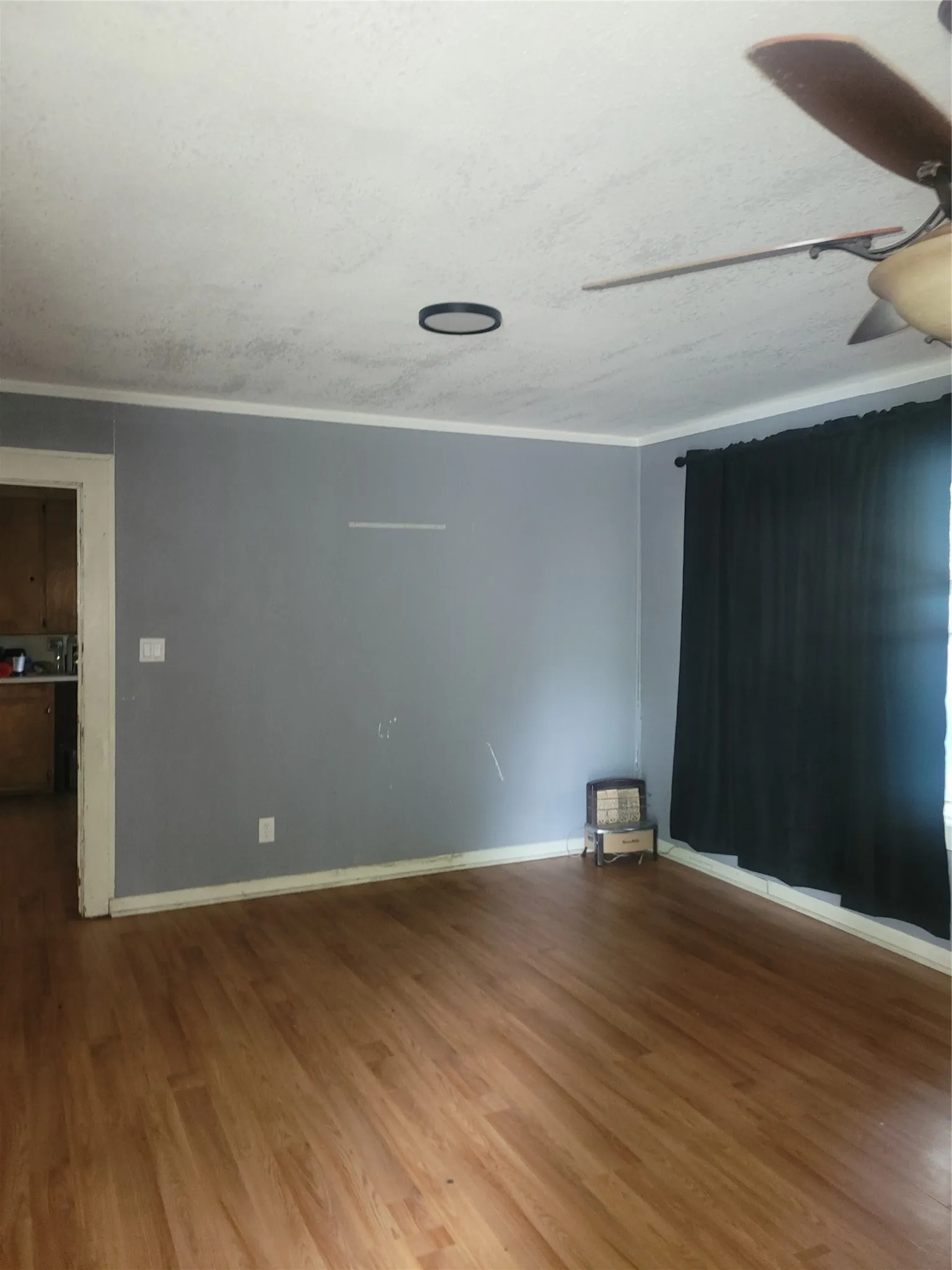 Spacious room featuring wood-finish flooring, a ceiling fan, and window with dark drapery