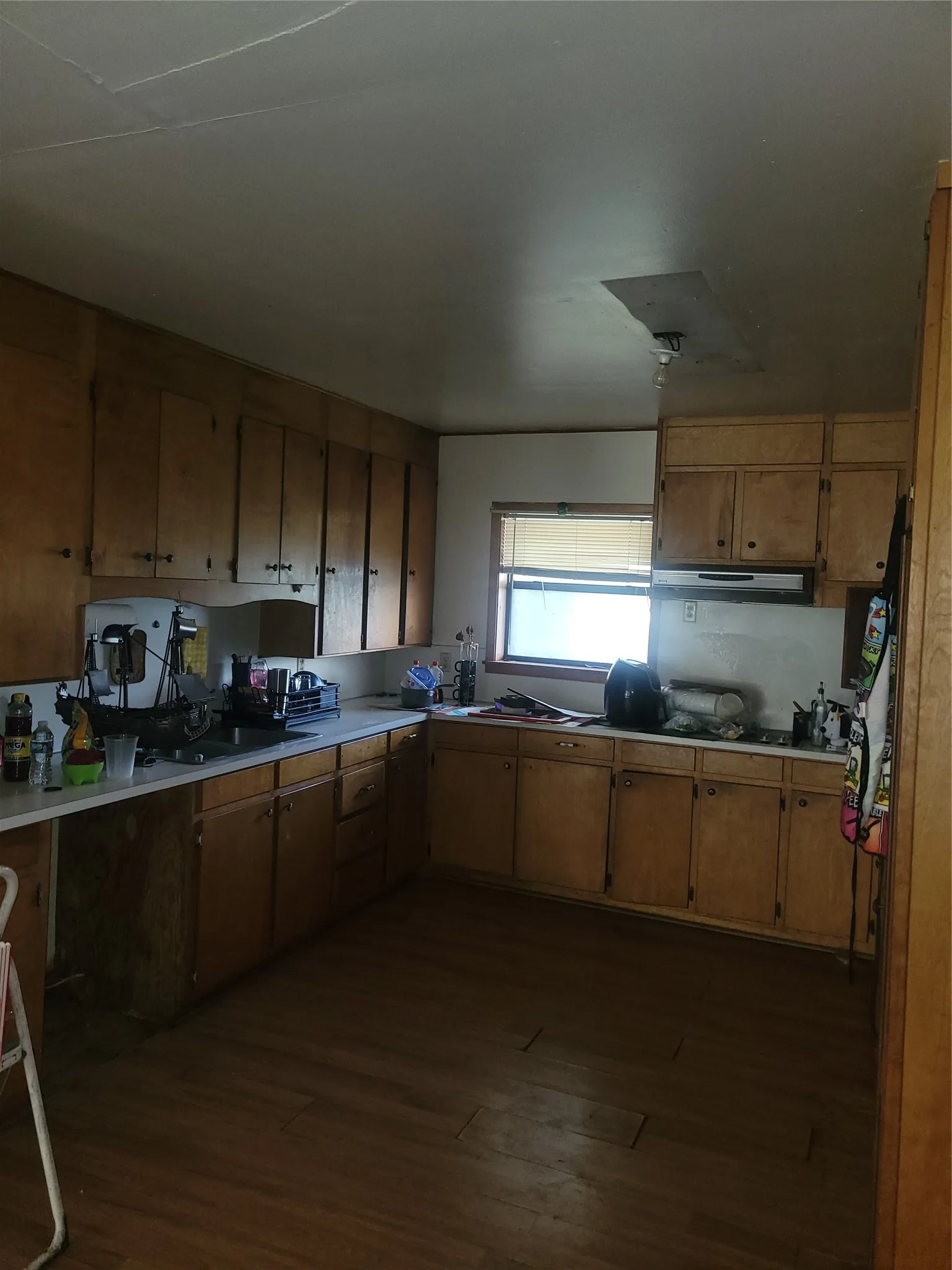 Kitchen featuring light wood cabinetry, a built-in range hood, a single window with blinds, and wood-finish flooring