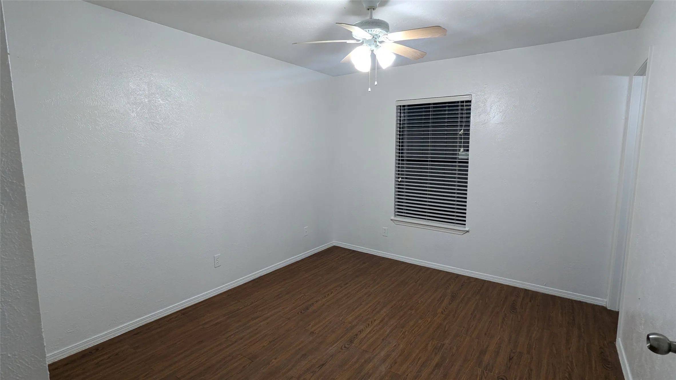 Wood-finish flooring, ceiling fan with light fixture, window with blinds, and white painted walls
