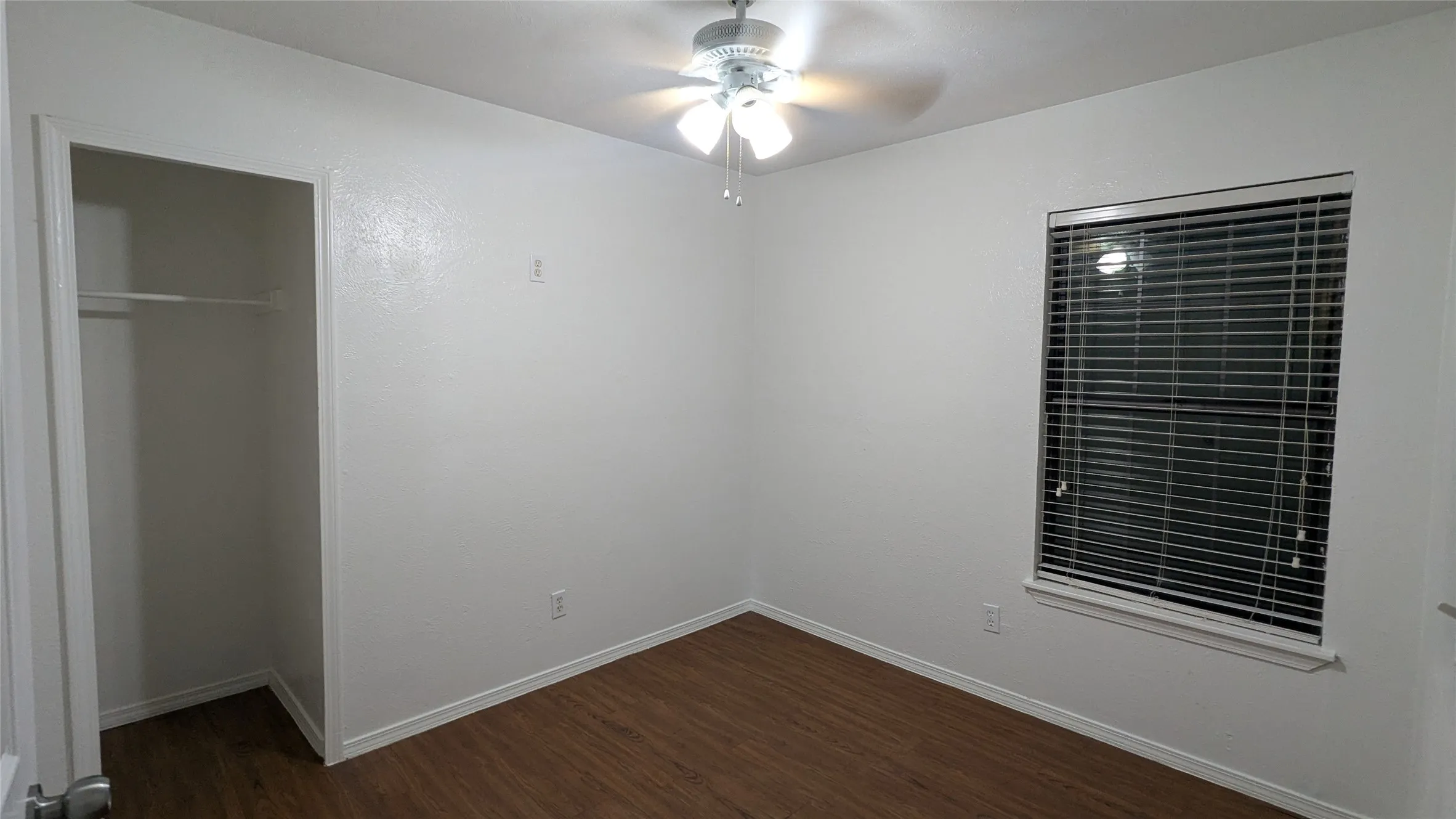Wood-finish flooring, white walls, ceiling fan with integrated lighting, window with blinds, and an open closet