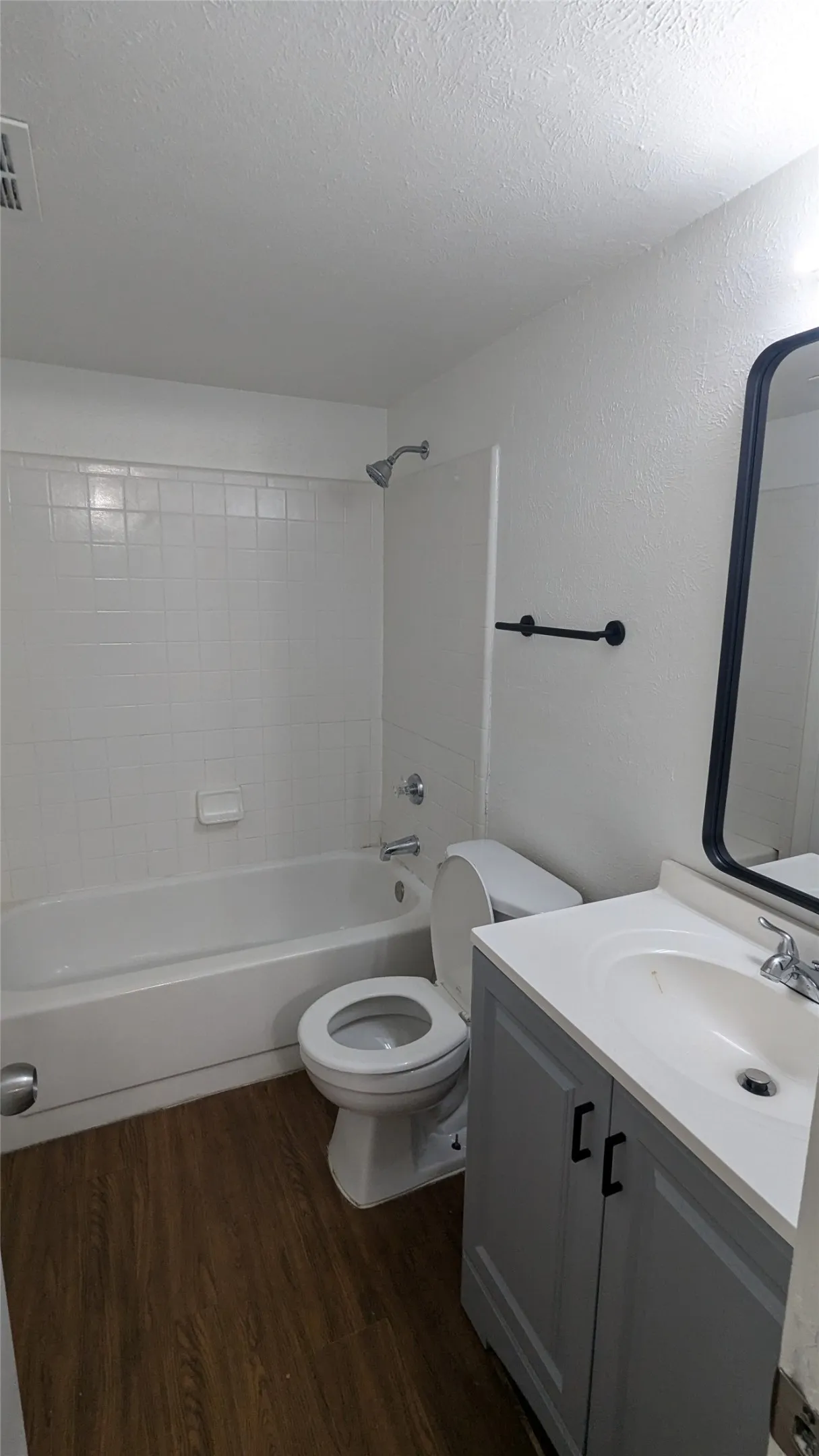 Bathroom featuring a white bathtub with subway tile surround, wood-finish flooring, and a vanity with a white countertop and gray cabinetry
