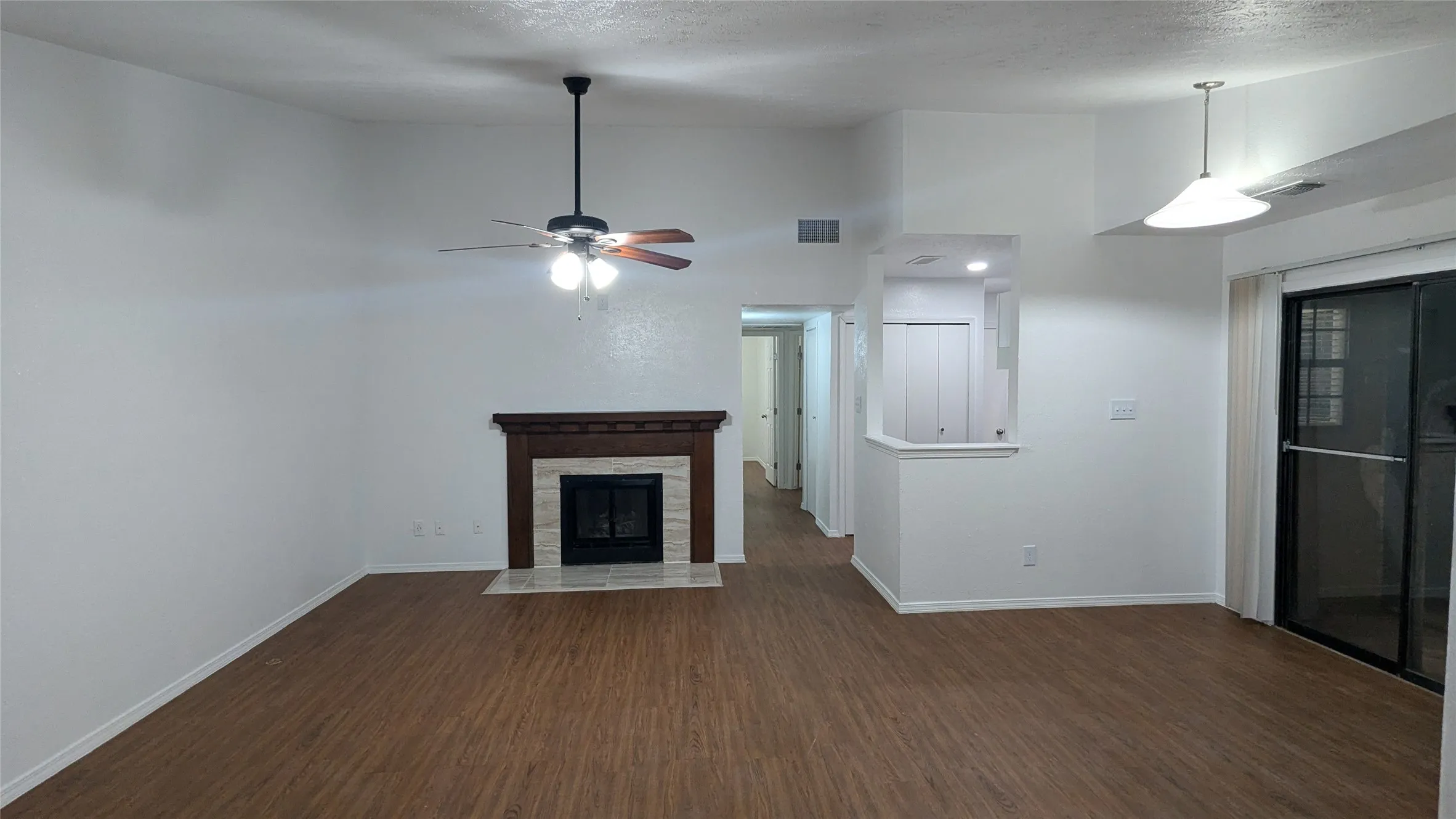 Living area with wood-finish flooring, vaulted ceiling, and a fireplace featuring a wood mantle and stone surround