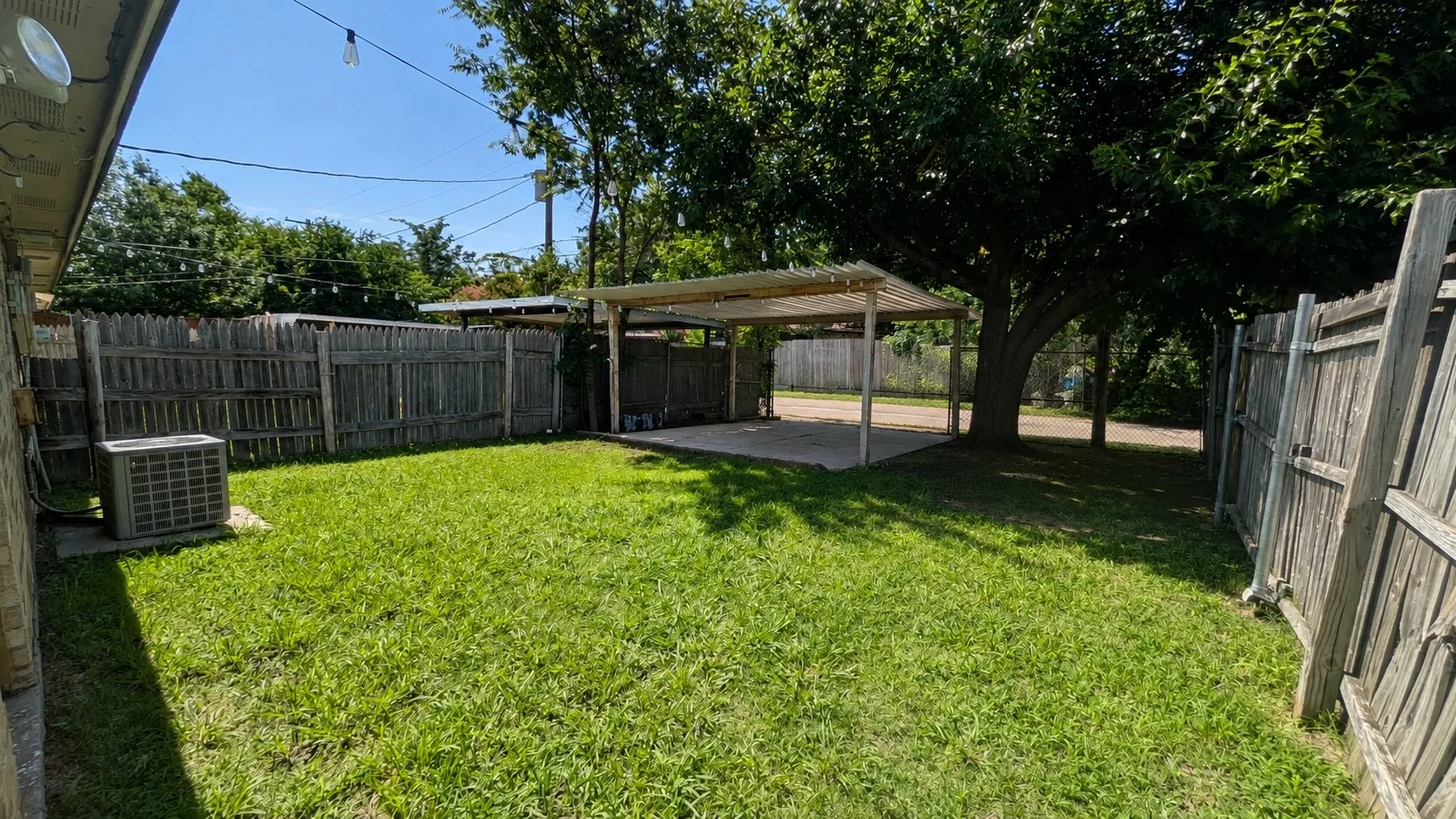 Expansive fenced backyard featuring a substantial covered patio, mature tree, and outdoor lighting