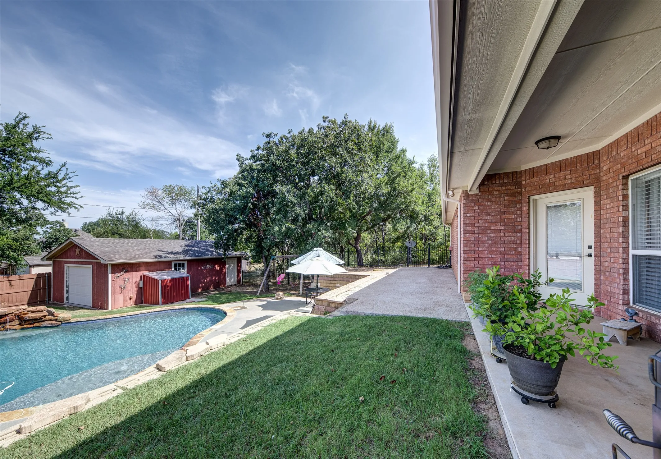 Brick exterior with covered patio, concrete pool deck, and fenced backyard