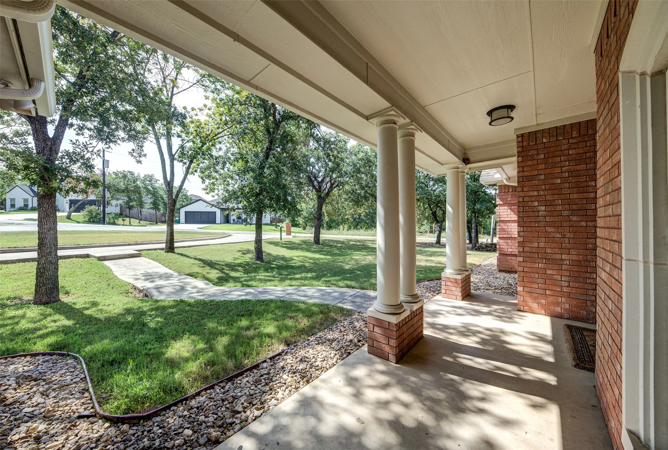 Brick exterior featuring a covered concrete porch, decorative columns with brick bases, and a ceiling-mounted light fixture