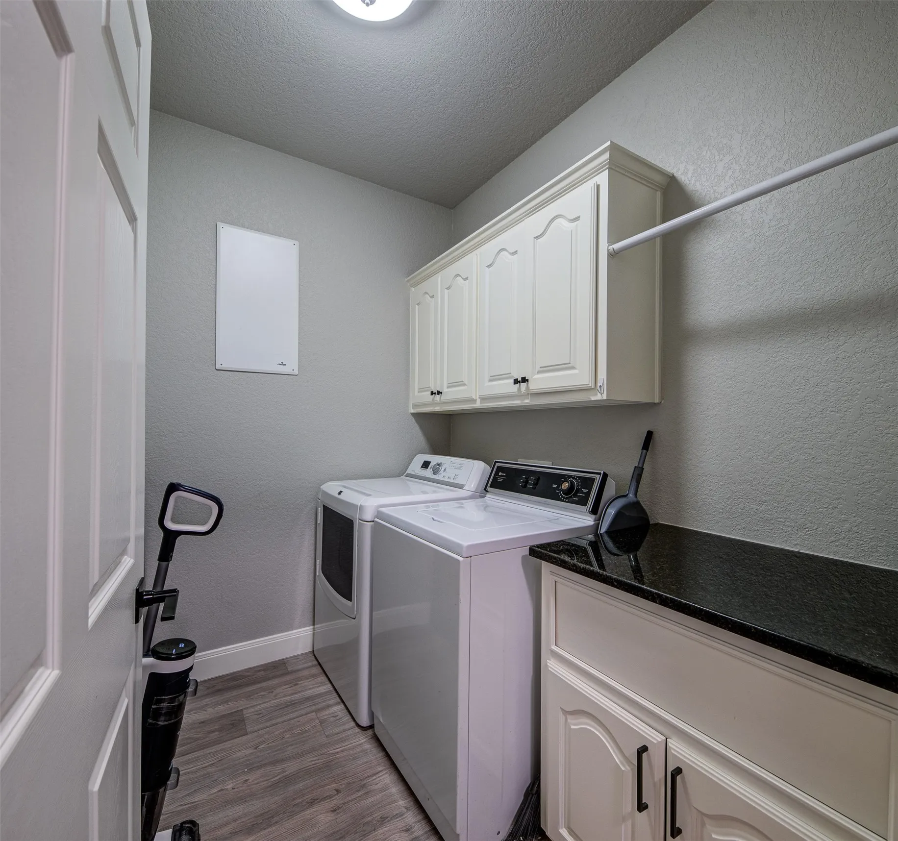 Laundry room with wood-finish flooring, overhead cabinetry, and a dark stone countertop