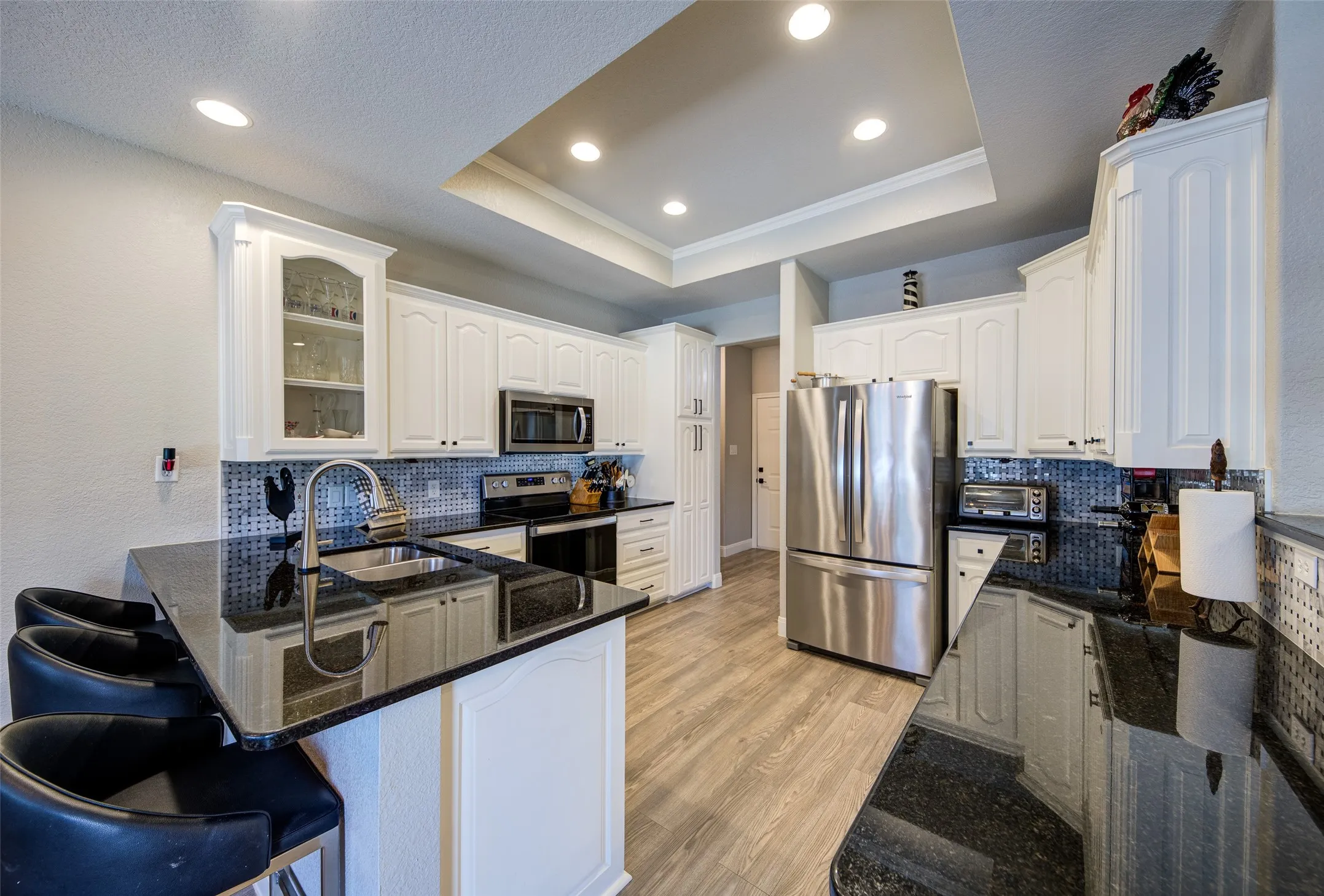 Kitchen featuring white cabinetry, stainless steel appliances, dark countertops, a tile backsplash, and light wood-finish flooring
