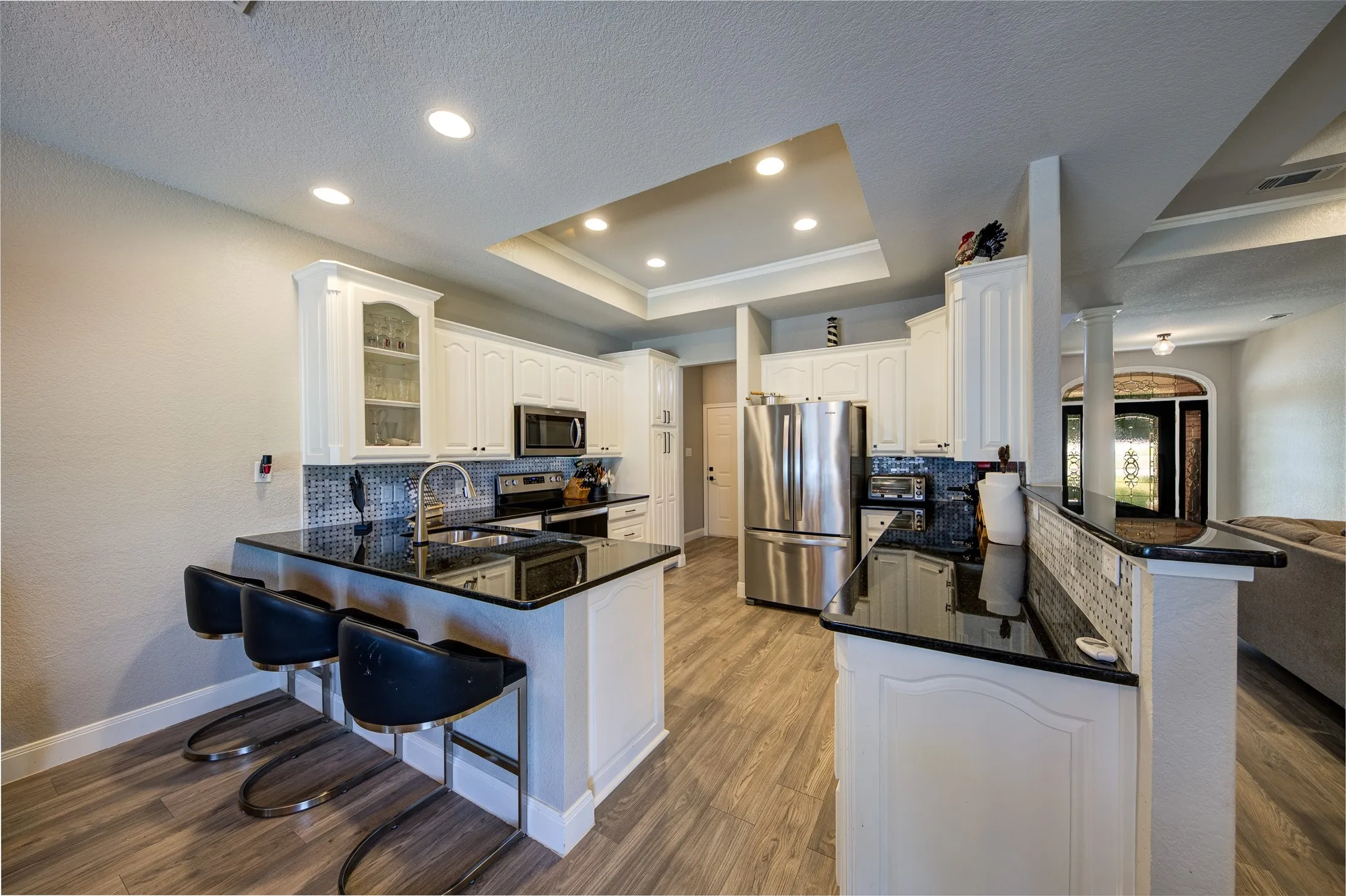 Kitchen featuring white cabinetry, breakfast bar, black countertops, stainless steel appliances, a tiled backsplash, and wood-finish flooring