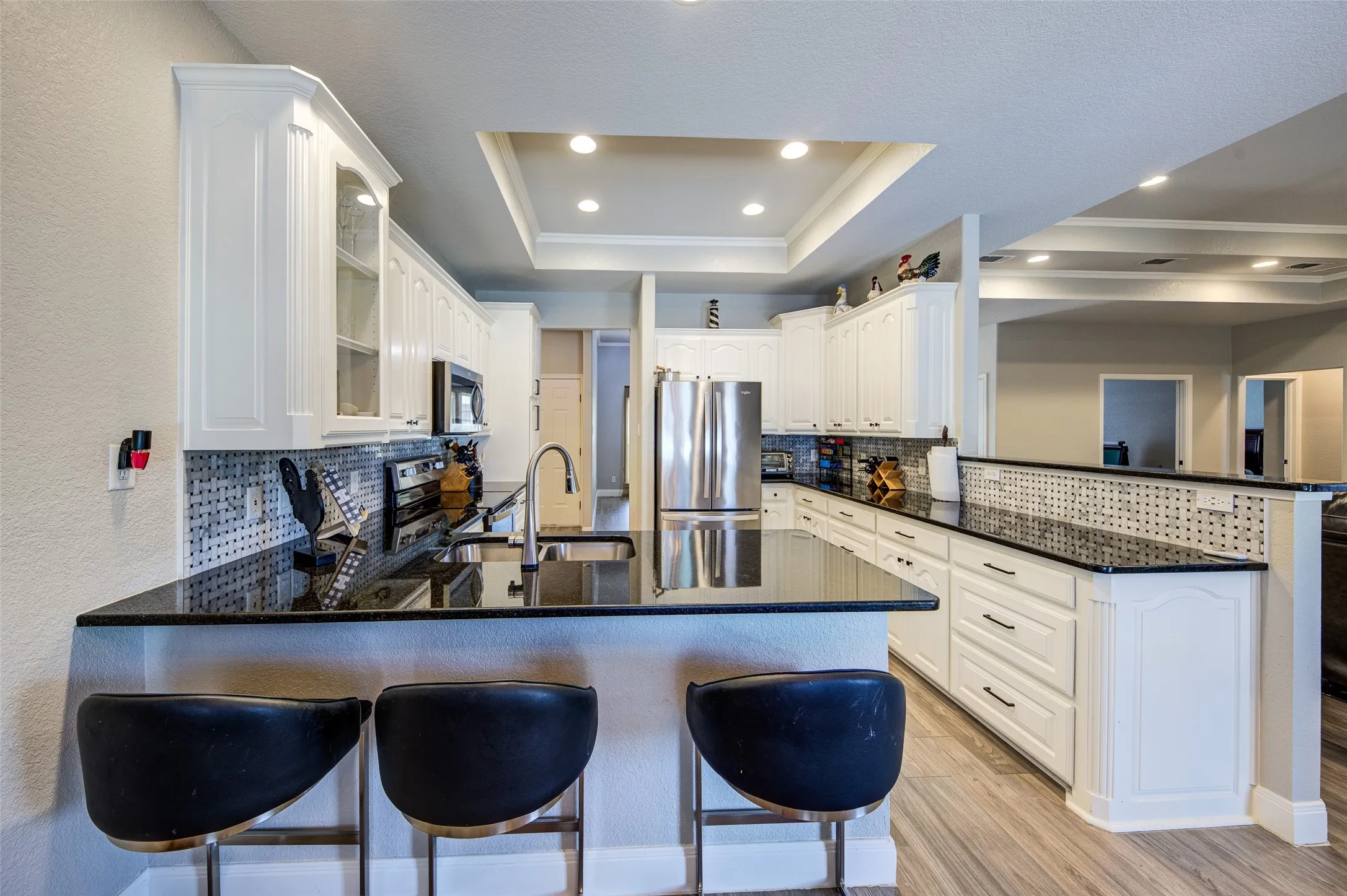 Kitchen featuring white cabinetry, dark countertops, breakfast bar, stainless steel appliances, a tiled backsplash, and recessed lighting