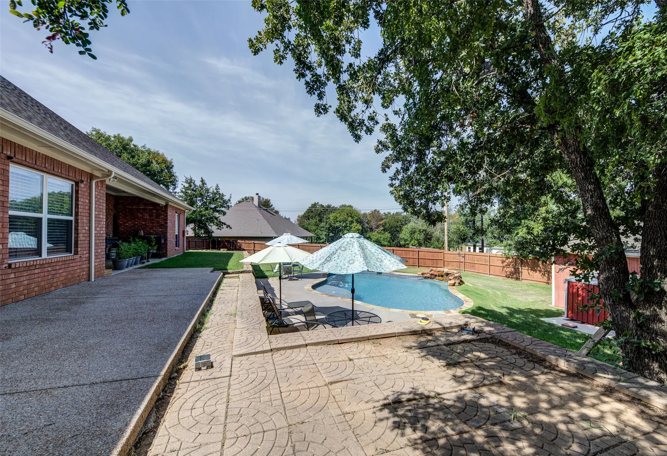 Brick exterior with covered patio, concrete pool deck, and fenced backyard