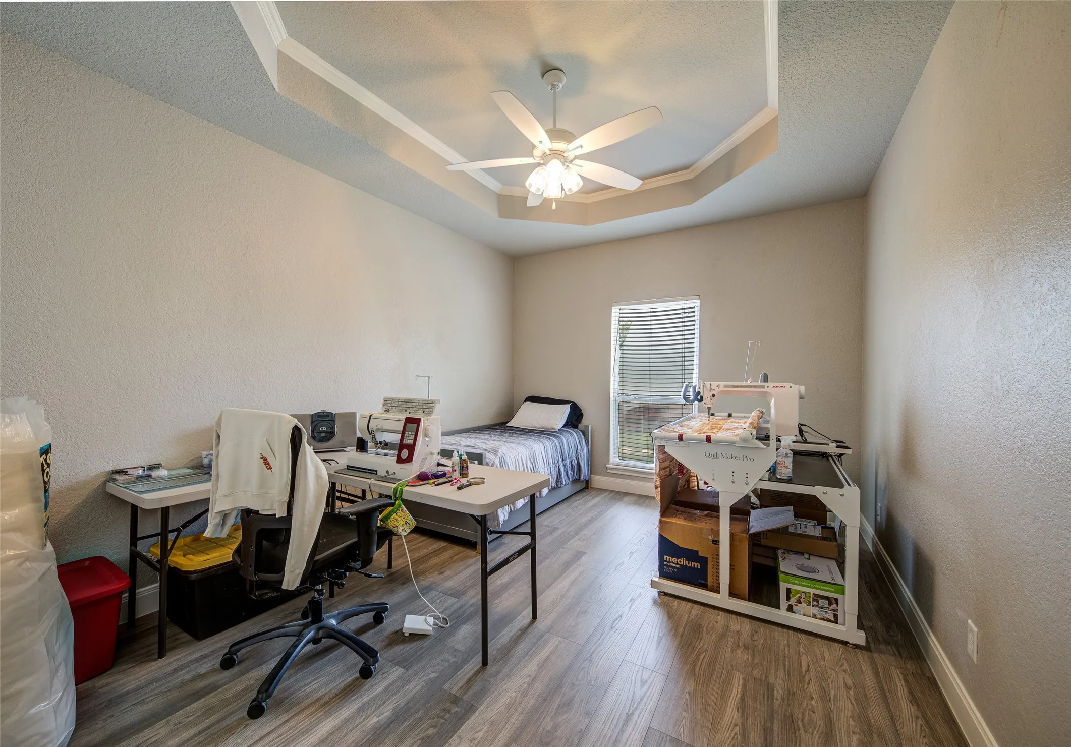 Tray ceiling with ceiling fan, wood-finish flooring, and a single window with blinds