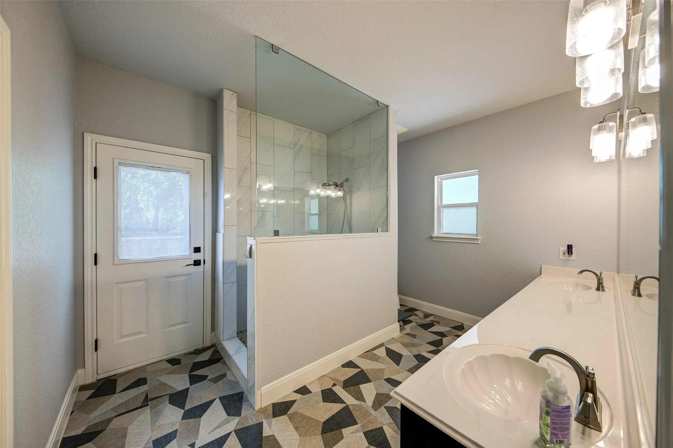 Contemporary bathroom with a dual vanity, glass-enclosed shower, patterned floor tile, and modern light fixtures