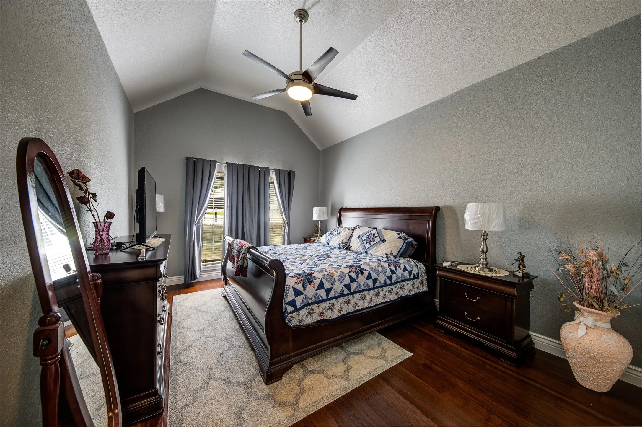 Vaulted ceiling with an attached ceiling fan, hardwood flooring, and multiple windows