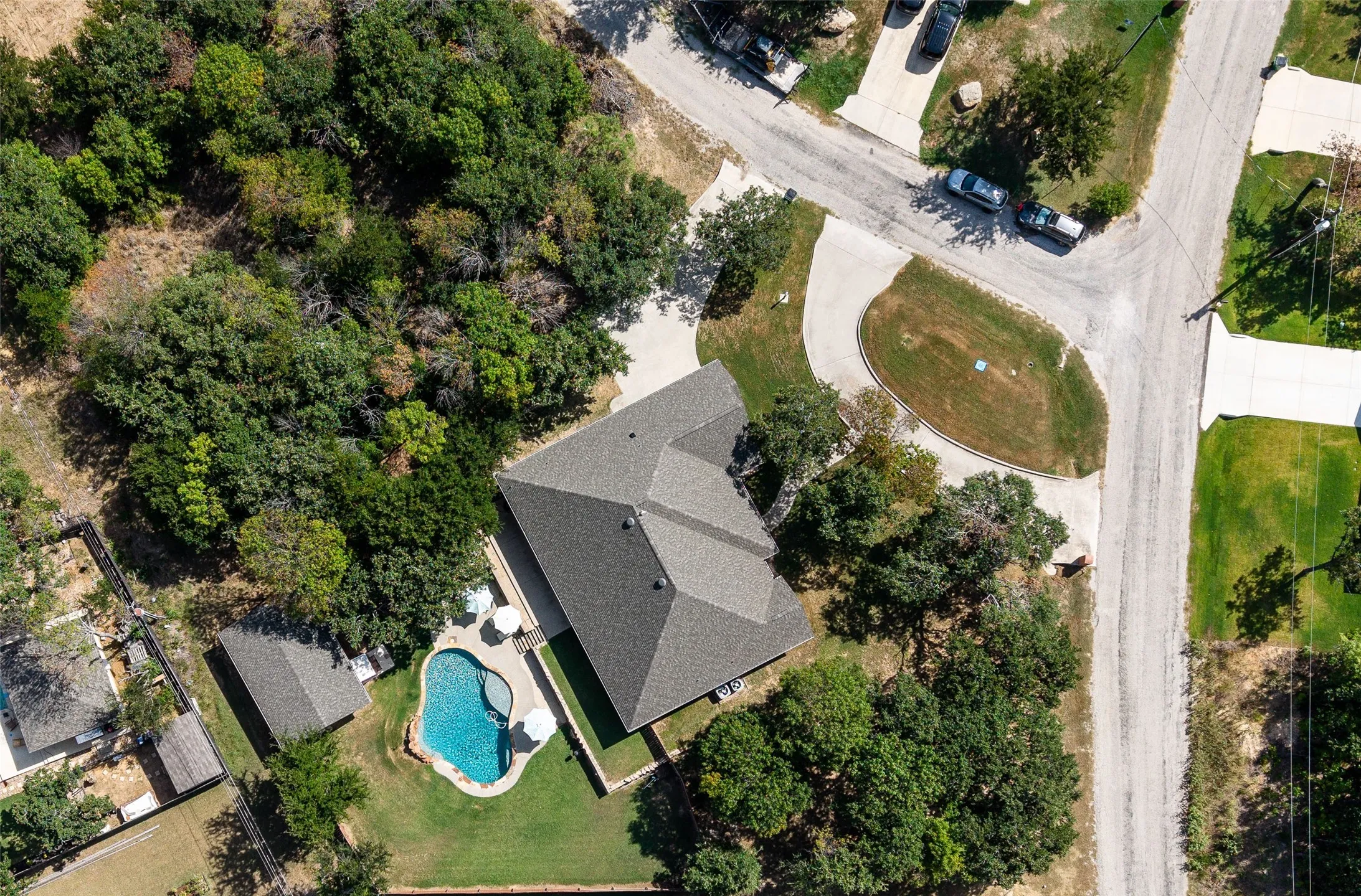 Asphalt shingle roof, swimming pool, detached structure, concrete patio, and extensive tree coverage