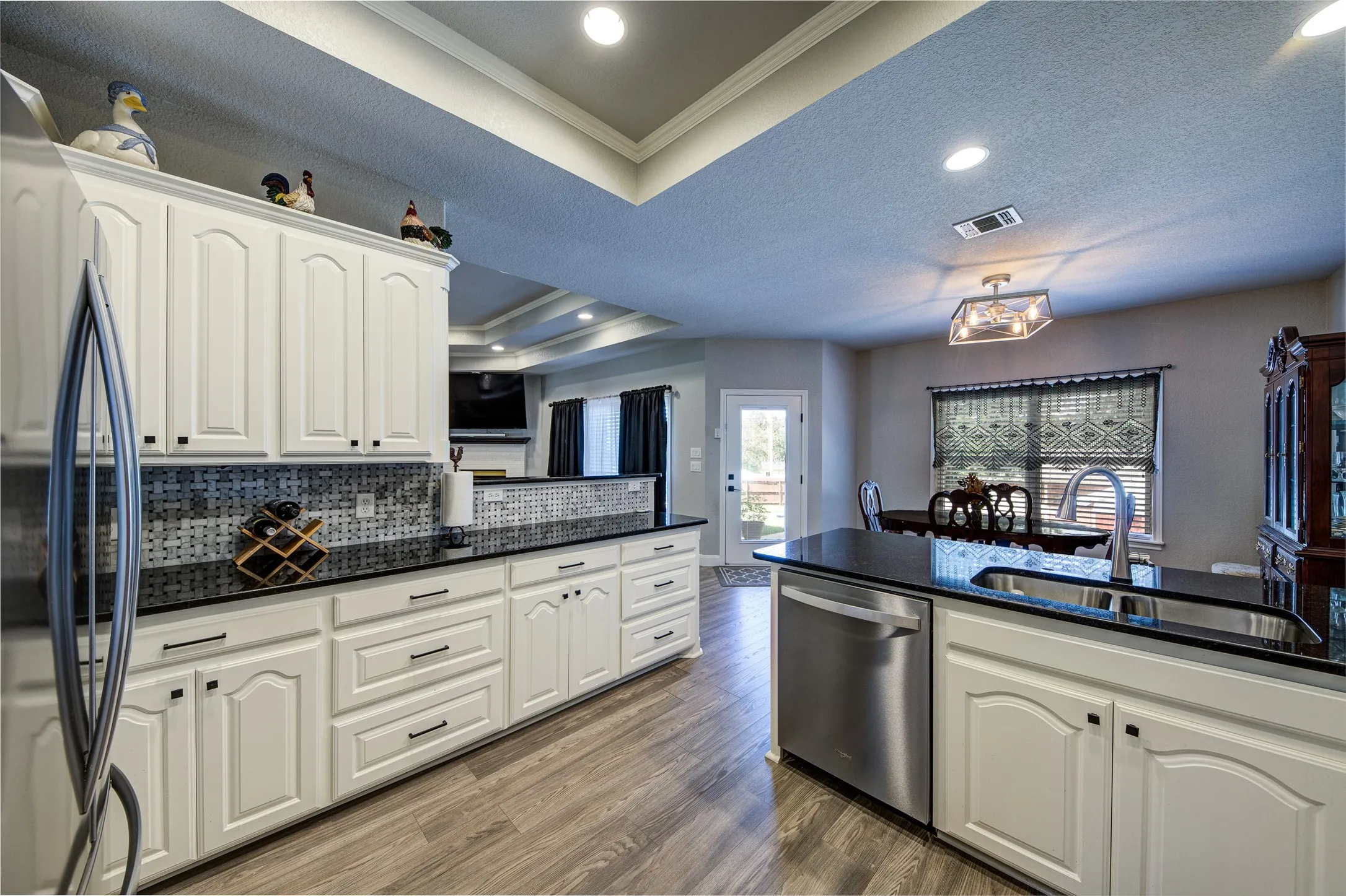 White cabinetry, dark countertops, wood-finish flooring, stainless steel appliances, and recessed lighting