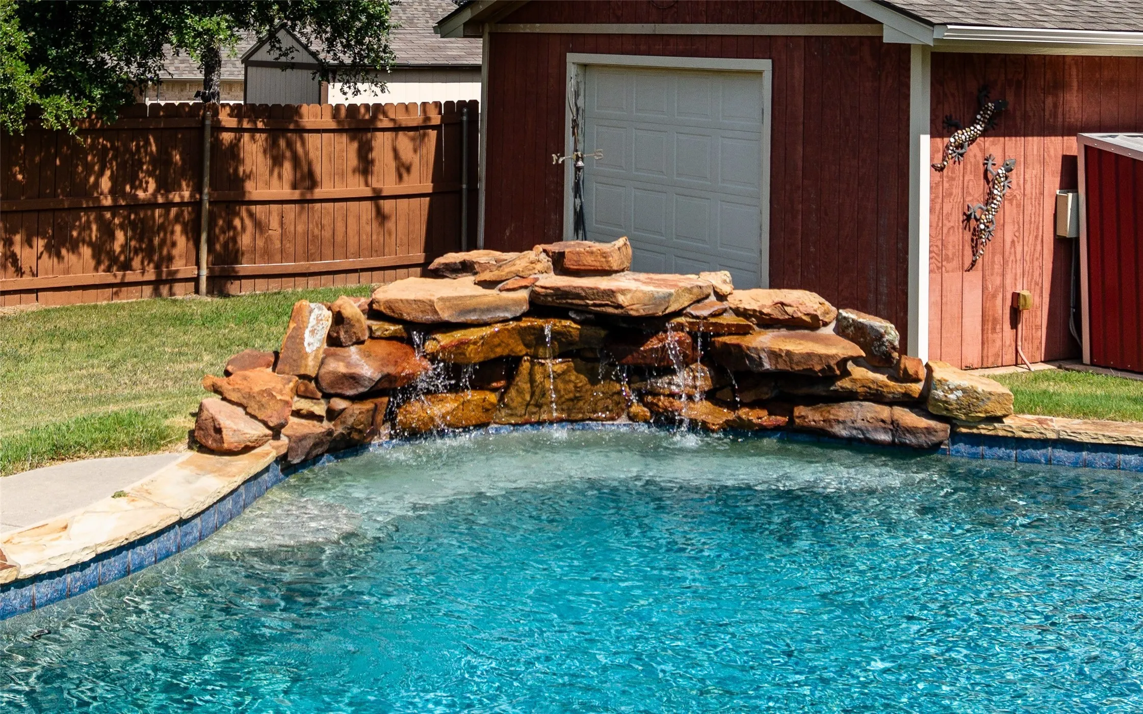 Swimming pool with a natural stone waterfall feature, blue tiled waterline, and concrete coping