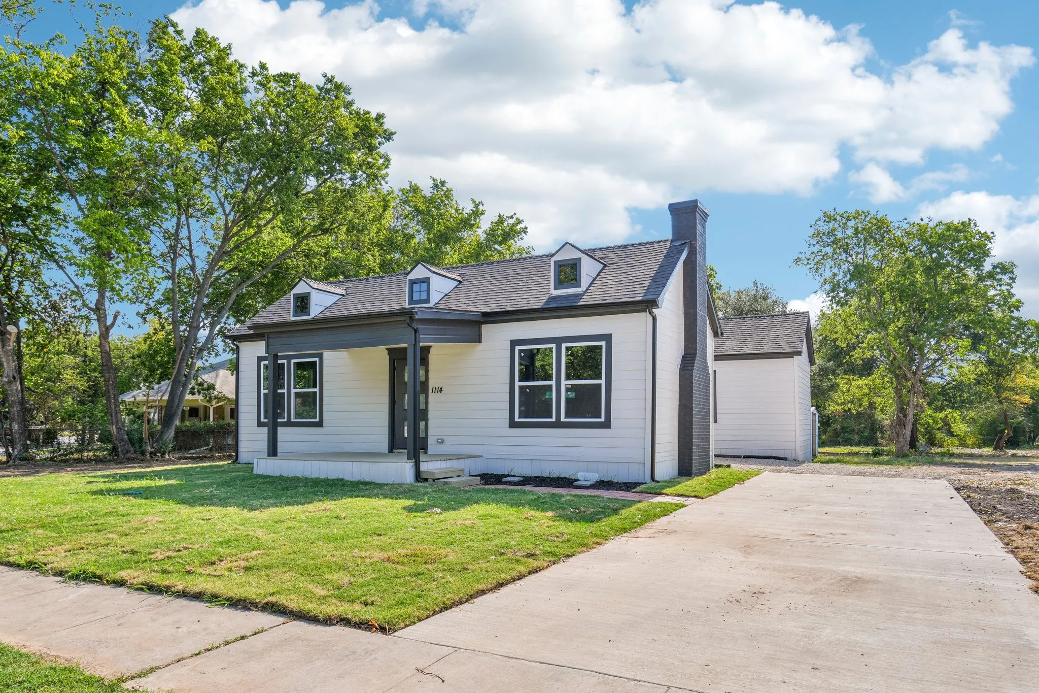 Siding exterior, covered front porch, dark-framed windows, prominent chimney, and a concrete driveway
