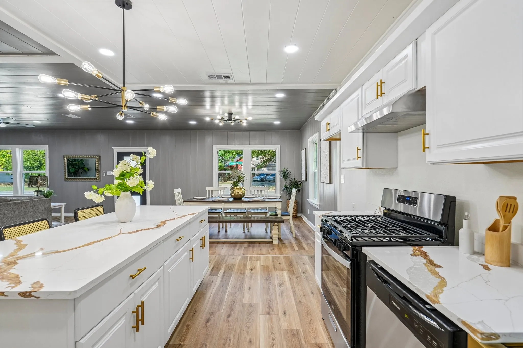 White shaker-style cabinetry with gold-tone hardware, stainless steel appliances, wood-finish flooring, white countertops with gold veining, and a contemporary light fixture
