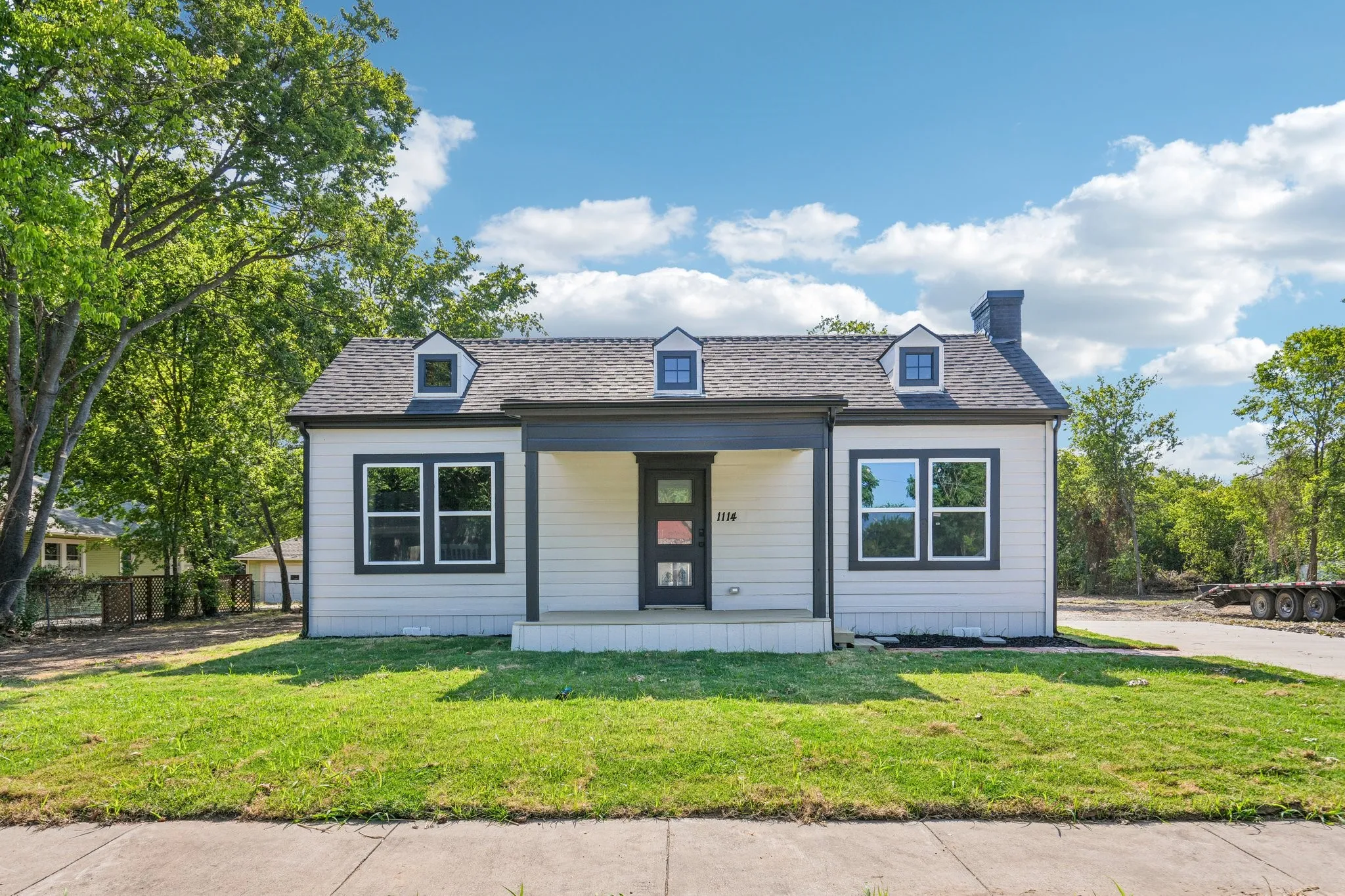 Siding exterior with dormer windows, covered front porch, and a dark-toned front door