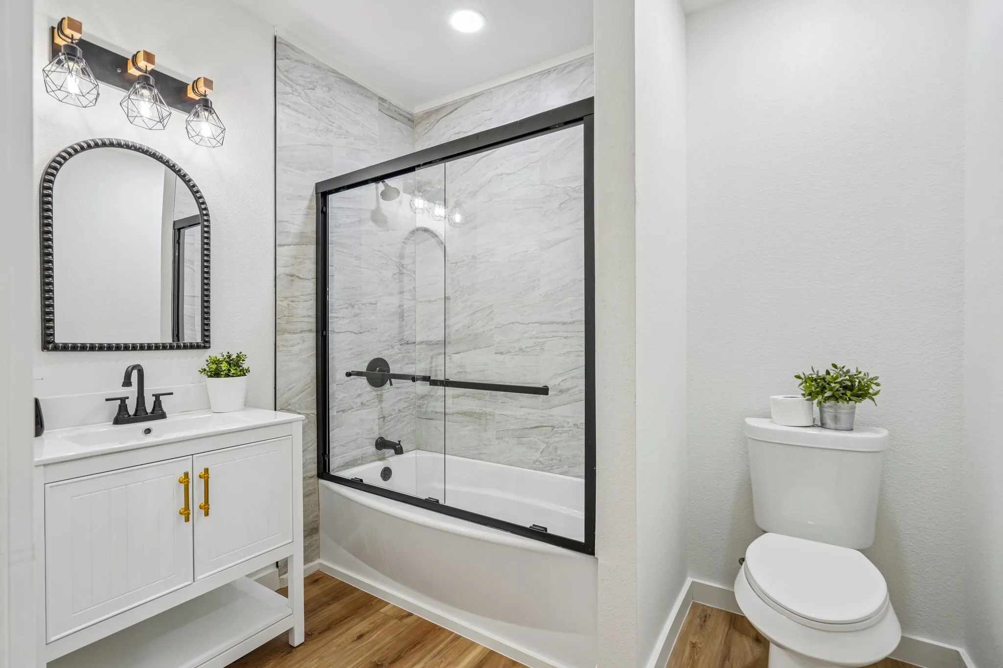 Bathroom featuring a white vanity with gold-tone hardware, a rectangular sink, matte black faucet, and an arched mirror